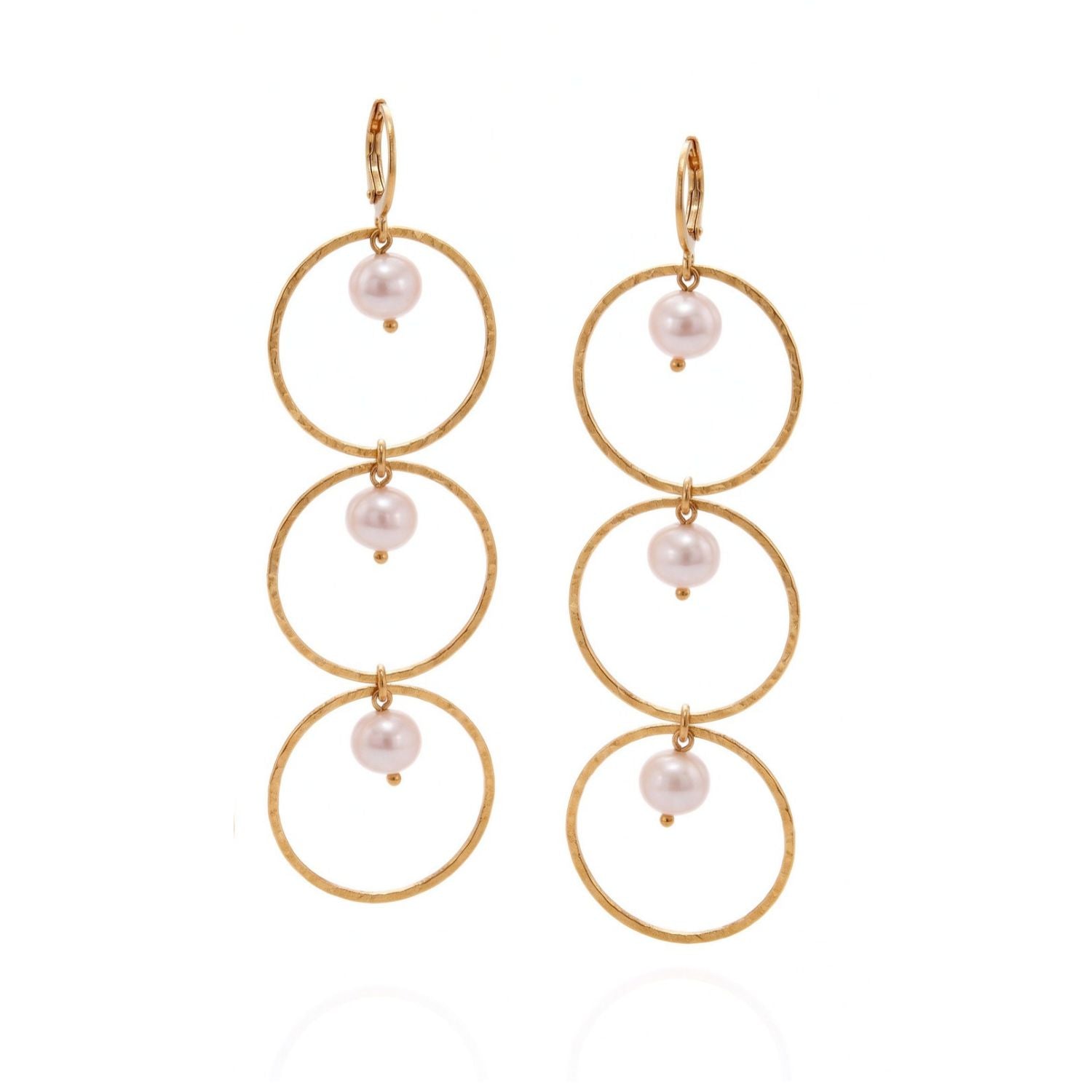 Pair of gold dangle earrings, each with three stacked thin hammered hoops joined by small white freshwater pearls, leverback hooks, side by side on a light gray background.