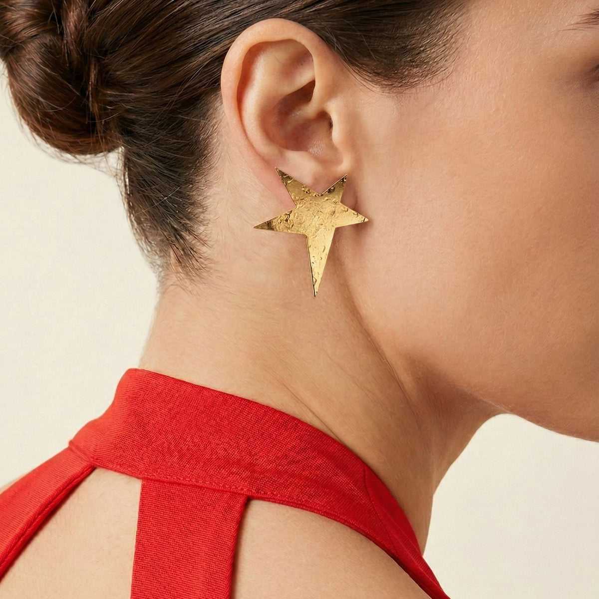 Close-up of a woman with a neat bun wearing Gold Shooting Star Stud Post Earrings by JAREDJAMIN Jewelry Online, styled with a sleeveless red top for a bold look against a plain background.