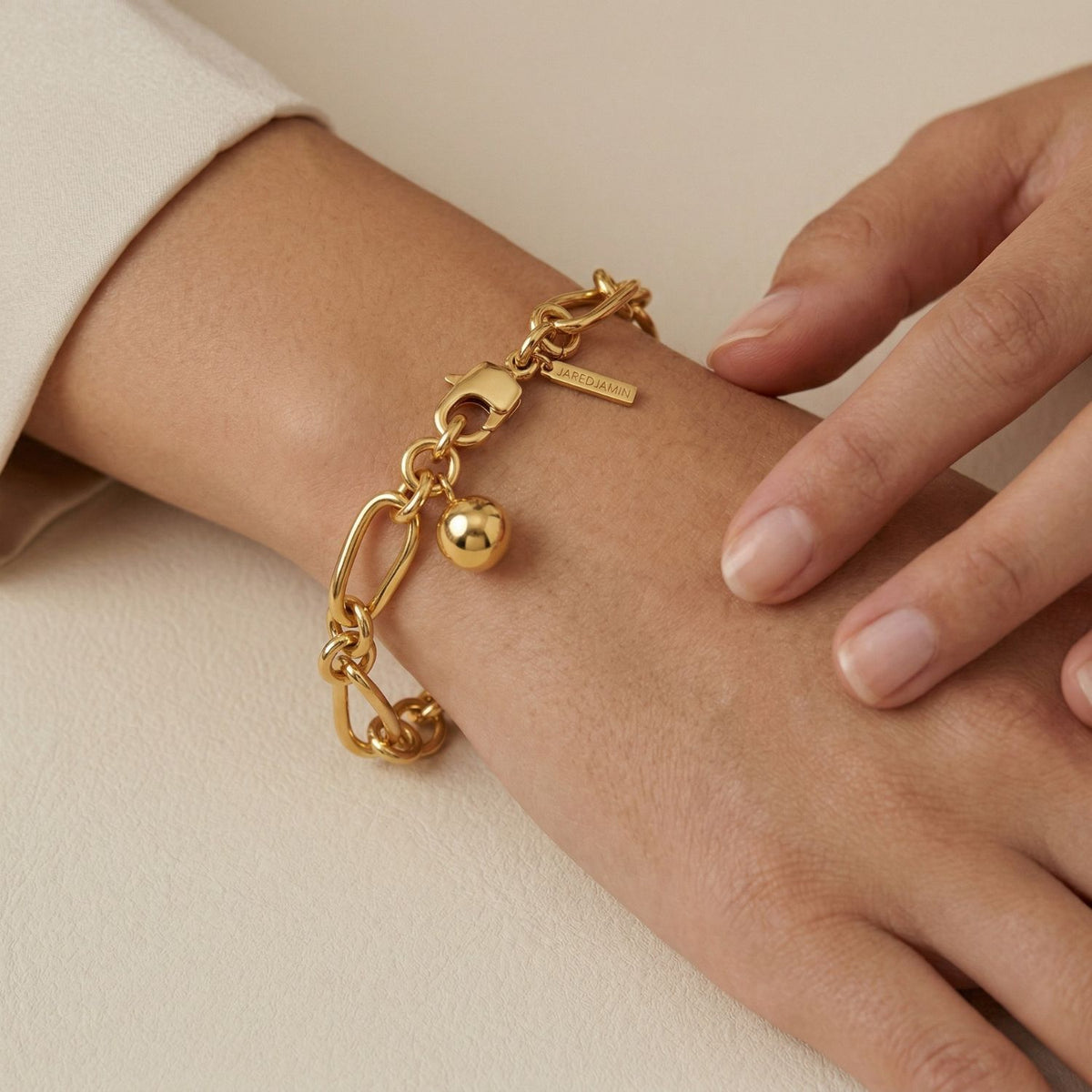 A close-up of a wrist punctuated by the Gold Skyler Chain Bracelet—sphere charm and rectangular tag suspended from hand-assembled links, crafted in our West Hollywood studio with small-batch care. Eco-conscious and tactile. Style Note: elevates denim, commands evening tailoring.