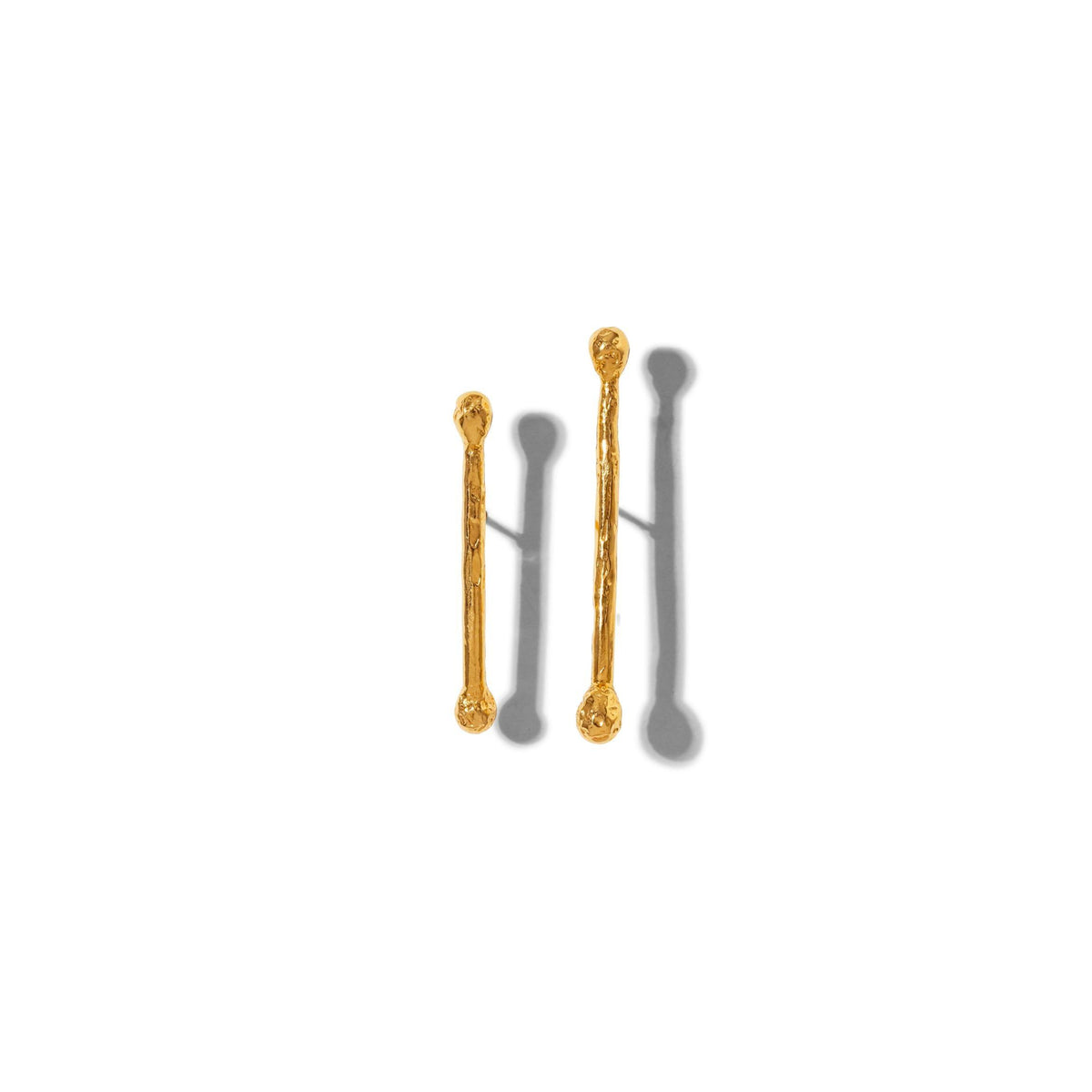 Les or Stix Post boucles d'oreilles par JAREDJAMIN Bijoux en Ligne présentent two texturé, or-colored metal sticks avec rounded ends et 18K or posts, arranged vertically on white to showcase their unique, organic surfaces et soft gray shadows.