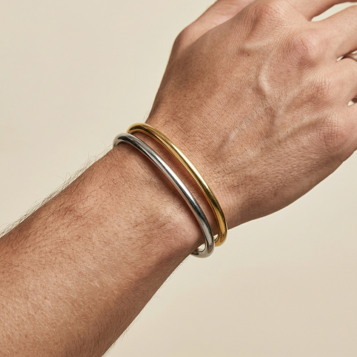 A close-up of a wrist adorned with the hand-assembled Gold Tubular Cuff and a minimalist silver bangle, each refracting soft light against a beige canvas. Mindfully crafted in small batches in our West Hollywood studio using eco-conscious methods. Style Note: punctuates everything from crisp shirting to silk evening sleeves.