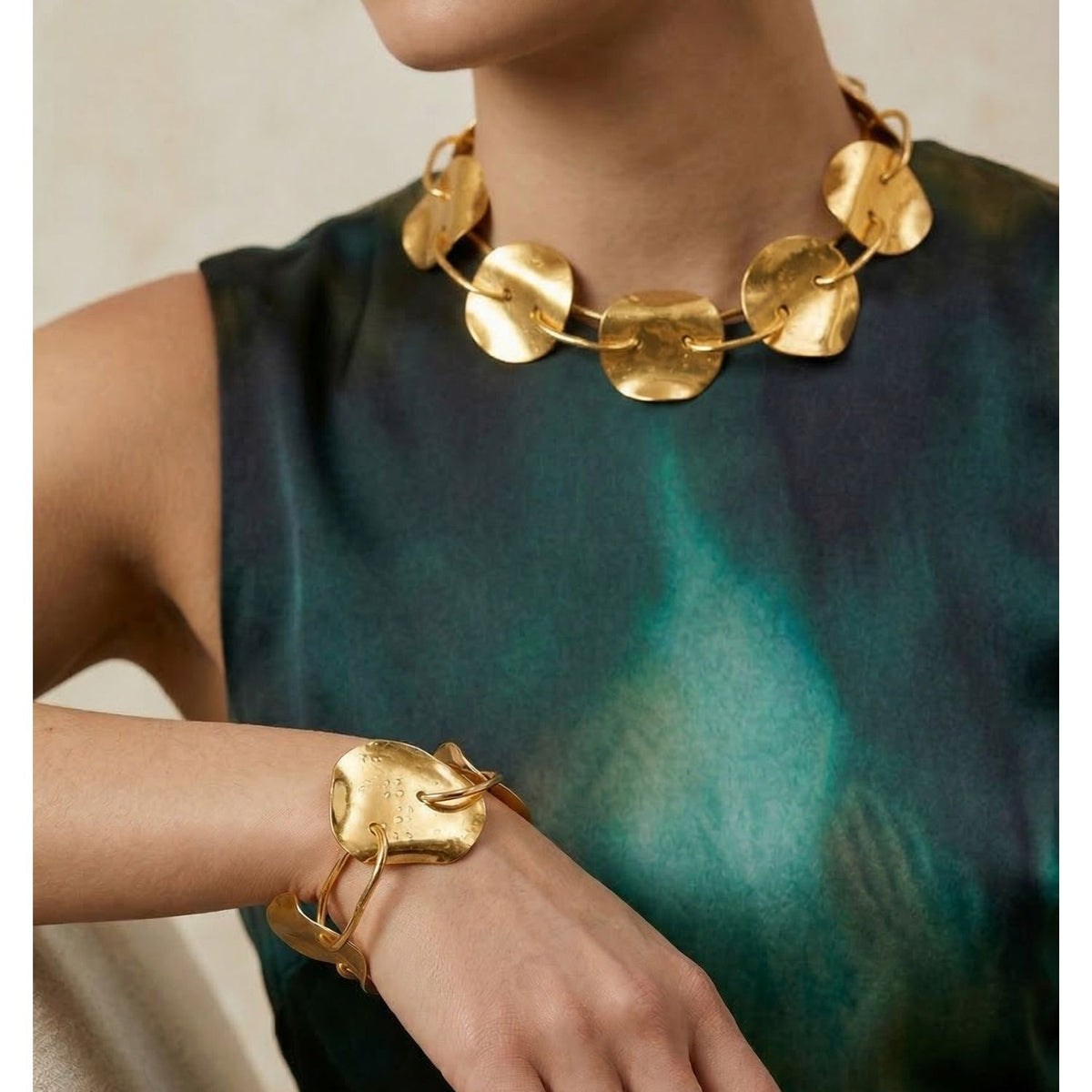 Bold, textured jewelry takes center stage: a chunky necklace and the gold Viviane Link Bracelet by JAREDJAMIN Jewelry Online, showcased on a model in a sleeveless teal-and-green dress against a neutral background.