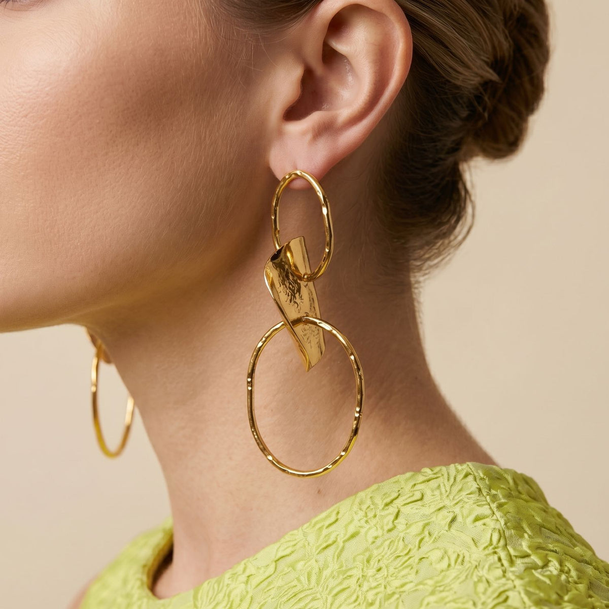Side-profile view of a model wearing the 4-inch Gold Viviane earrings, demonstrating their dramatic jawline scale, fluid metallic movement, and reflective organic texture paired with a chartreuse dress.