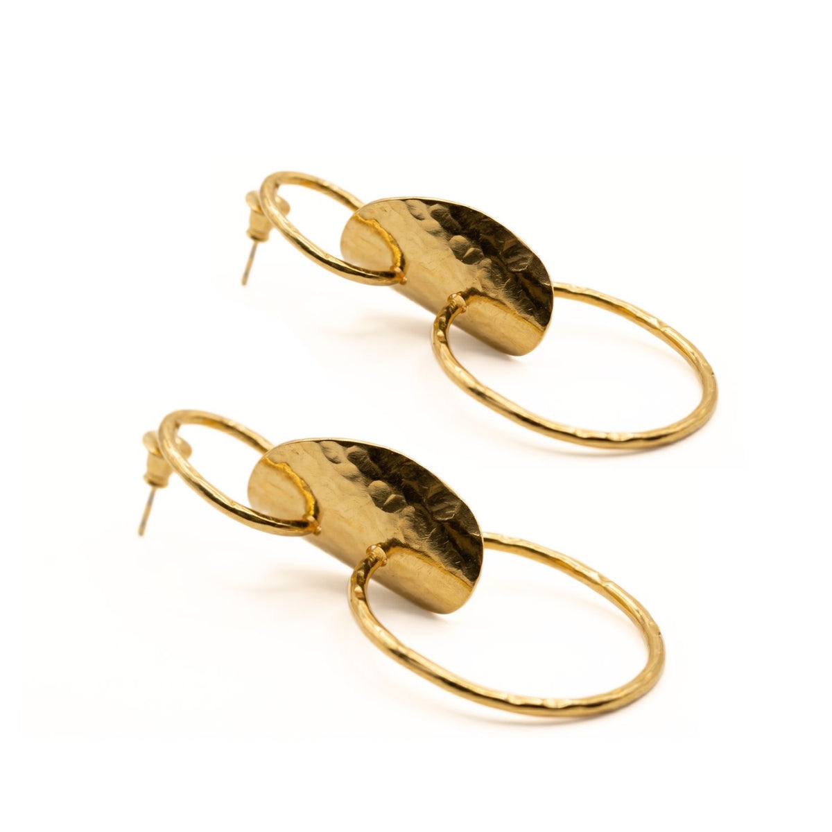Angled layout view of the Gold Viviane earrings resting on a white surface, showcasing the secure ear posts, the depth of the wavy central disc contours, and the signature hammered finish.