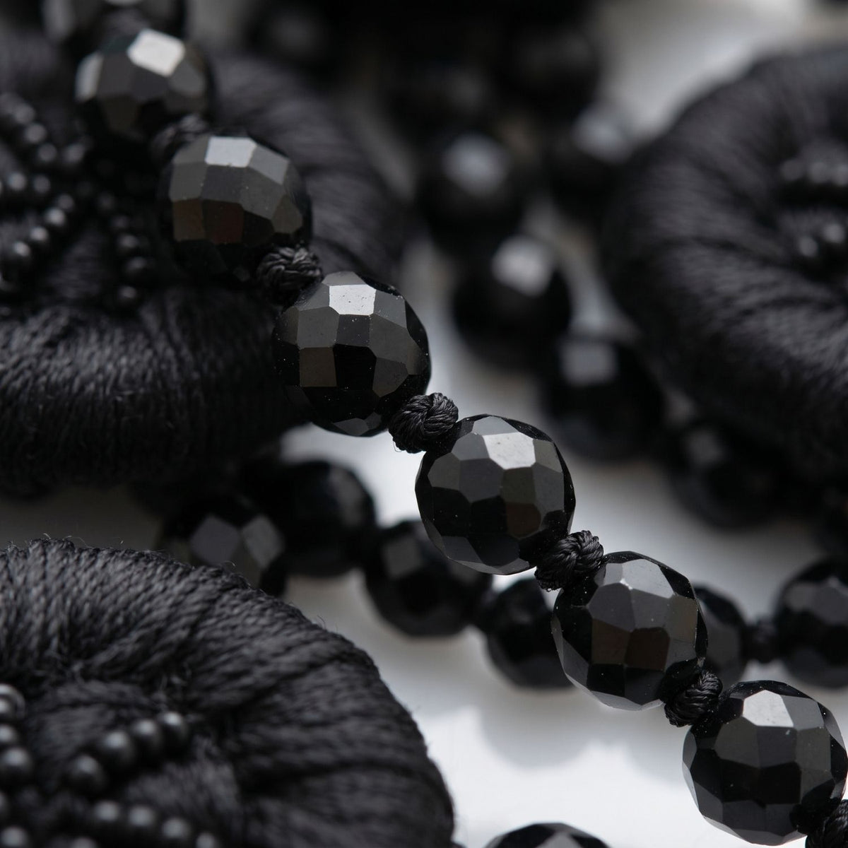 Sharp macro studio shot focusing tightly on the intricate details of the Good Mourning Victoria Necklace, showcasing the tactile contrast between the shiny faceted black glass beads and the matte, hand-beaded satin wrapped around the vintage buttons.
