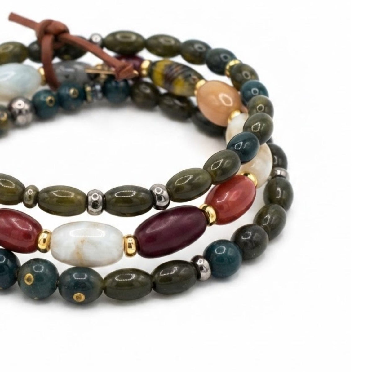 Close-up studio shot of the Silvan bracelet stack focusing on the football-shaped oval glass and quartz beads, gold-plated hematite discs, and green oblong wood texture.
