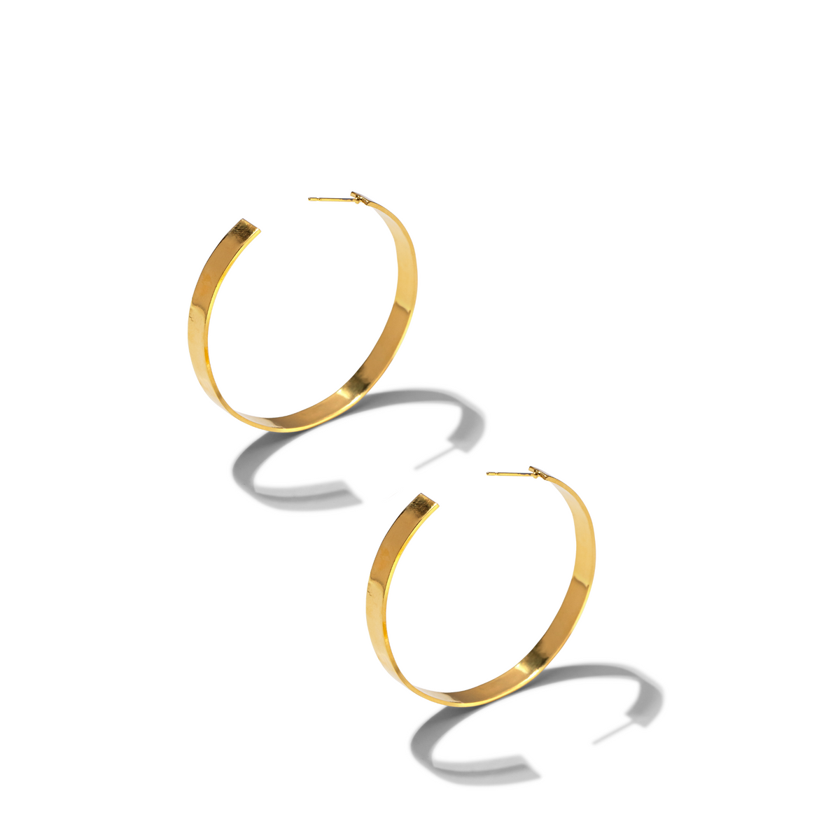 Les Heather créole Post boucles d'oreilles de JAREDJAMIN Bijoux en Ligne, avec flat, wide 18K plaqué or surfaces, rest sur un fond blanc. Each créole casts a soft curved shadow that highlights their élégant metallic shine.