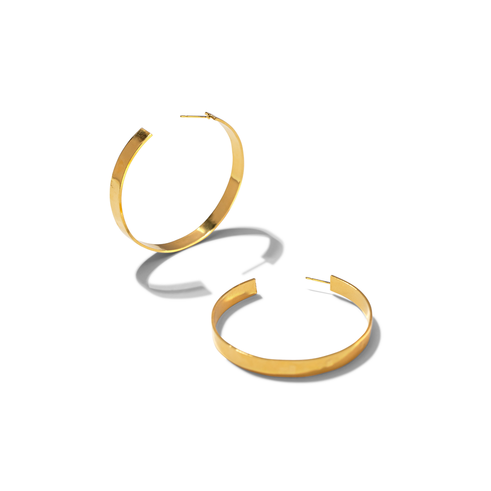 The Heather Hoop Post Earrings by JAREDJAMIN Jewelry Online feature shiny 18K gold plated, flat wide bands. Resting on a white surface, each lightweight earring is open at the clasp and casts a soft gray shadow, highlighting their polished finish.