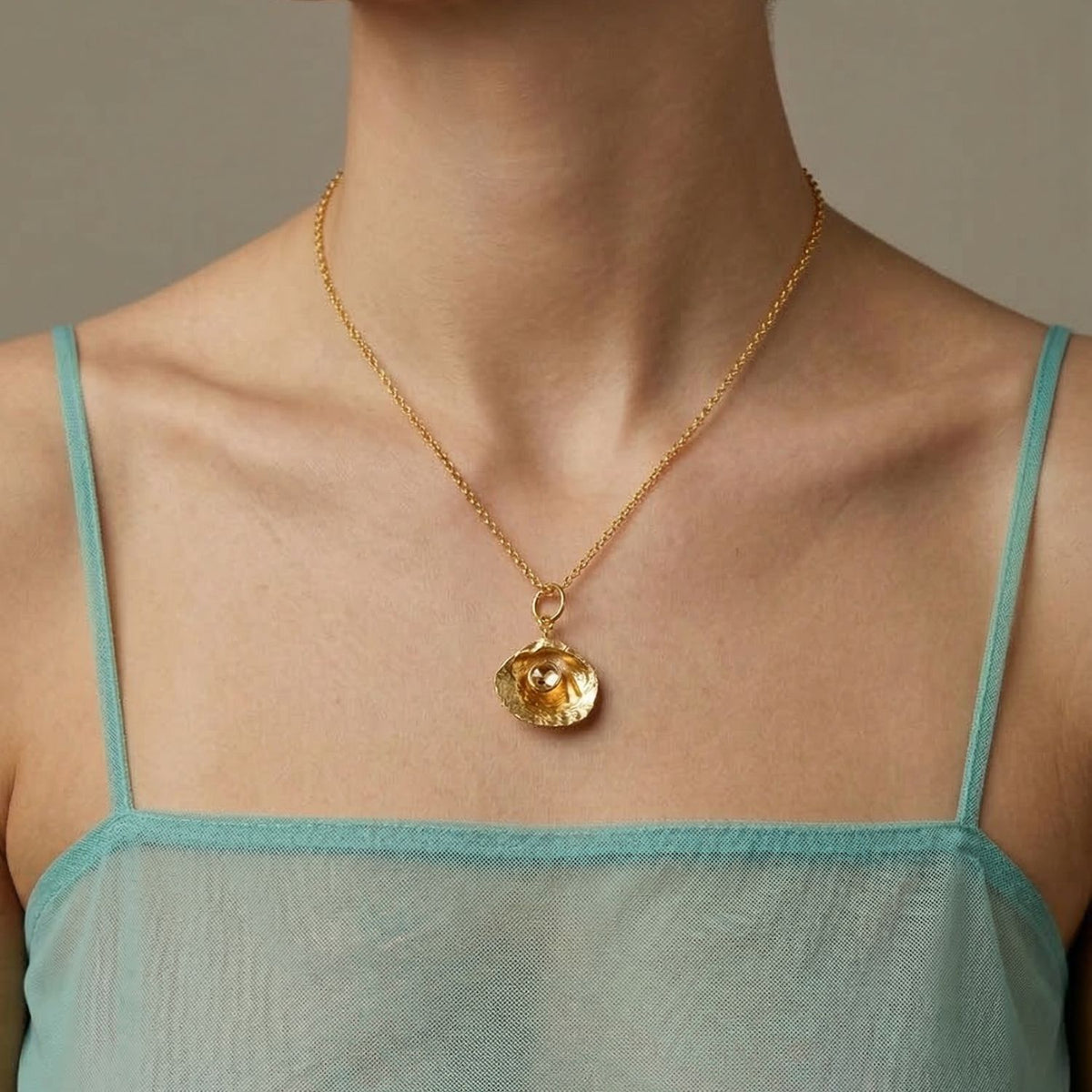 Un person wears a sheer teal spaghetti-strap top y the Hidden Glimmer colgante collar de JAREDJAMIN Joyería Online. Los focus is en el neck, collarbone, y upper chest against a neutral background.