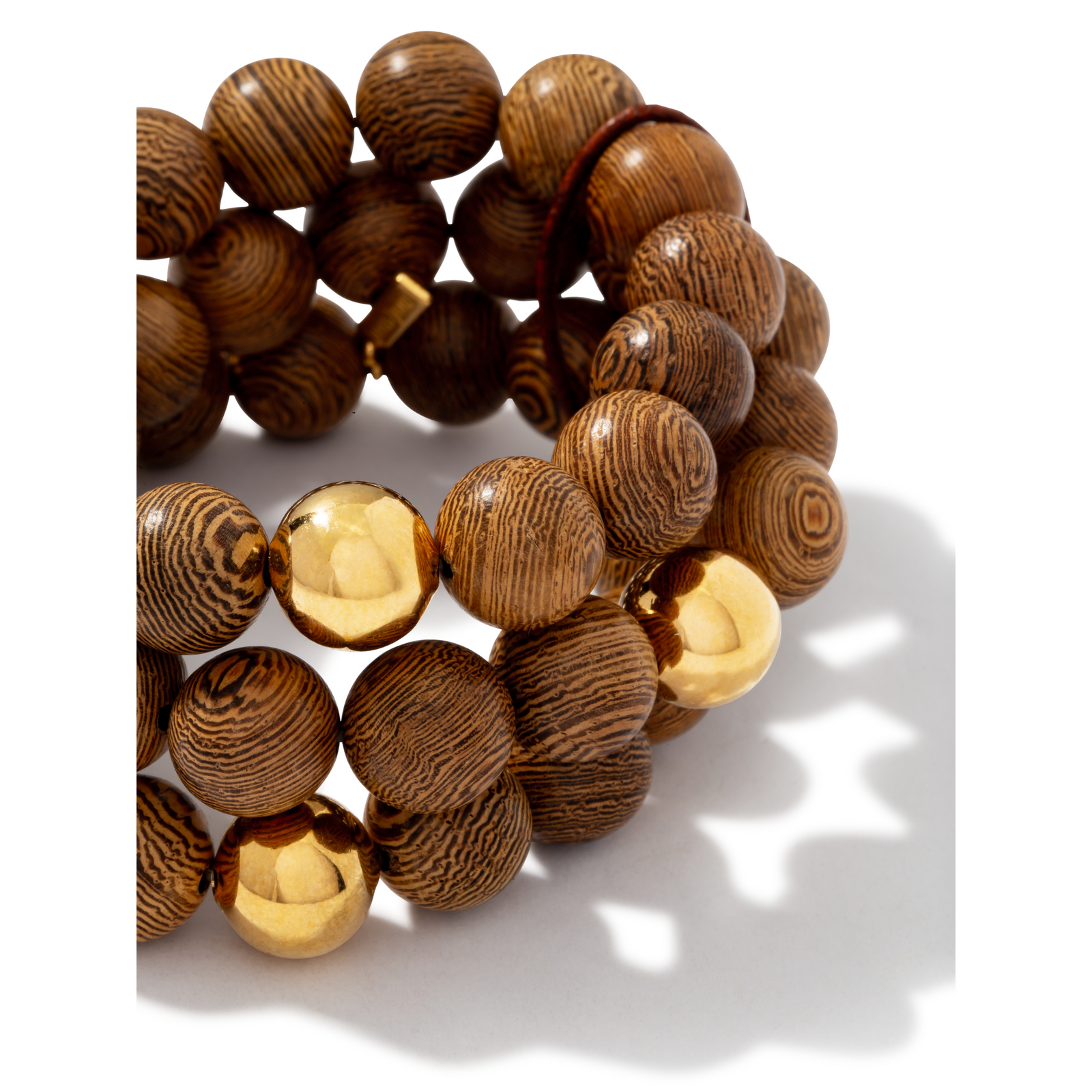 The Into The Woods Bracelet from JAREDJAMIN Jewelry Online features three coiled strands of round, patterned sandalwood beads with 18K gold accents, displayed on a white background with a soft shadow to the right.