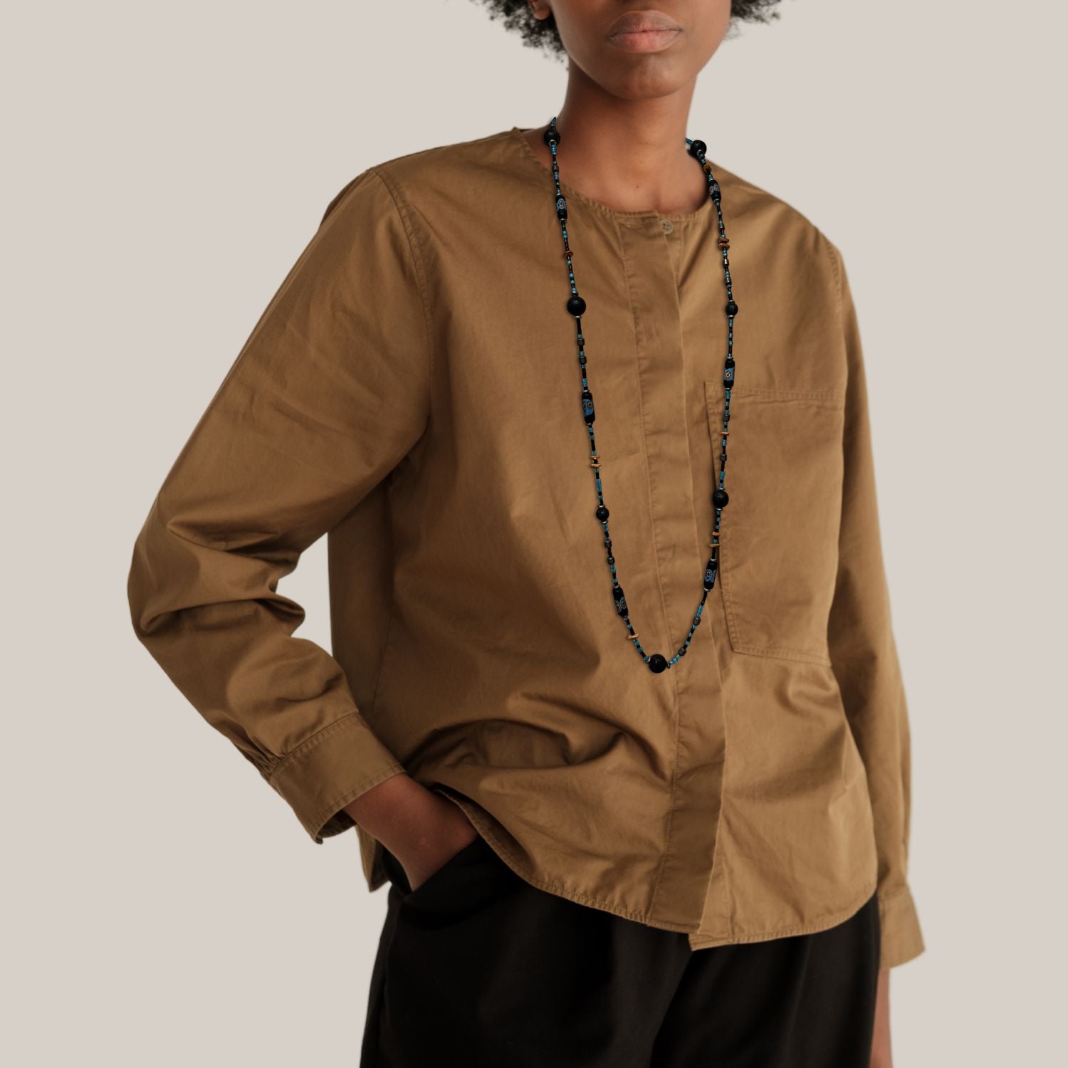 The African Voyage Long Lava Necklace by JAREDJAMIN Jewelry Online features three vintage strands with black lava, hematite, blue hand-painted African glass beads with floral patterns, sky-blue and black seed beads, tan discs, and a silver clasp.