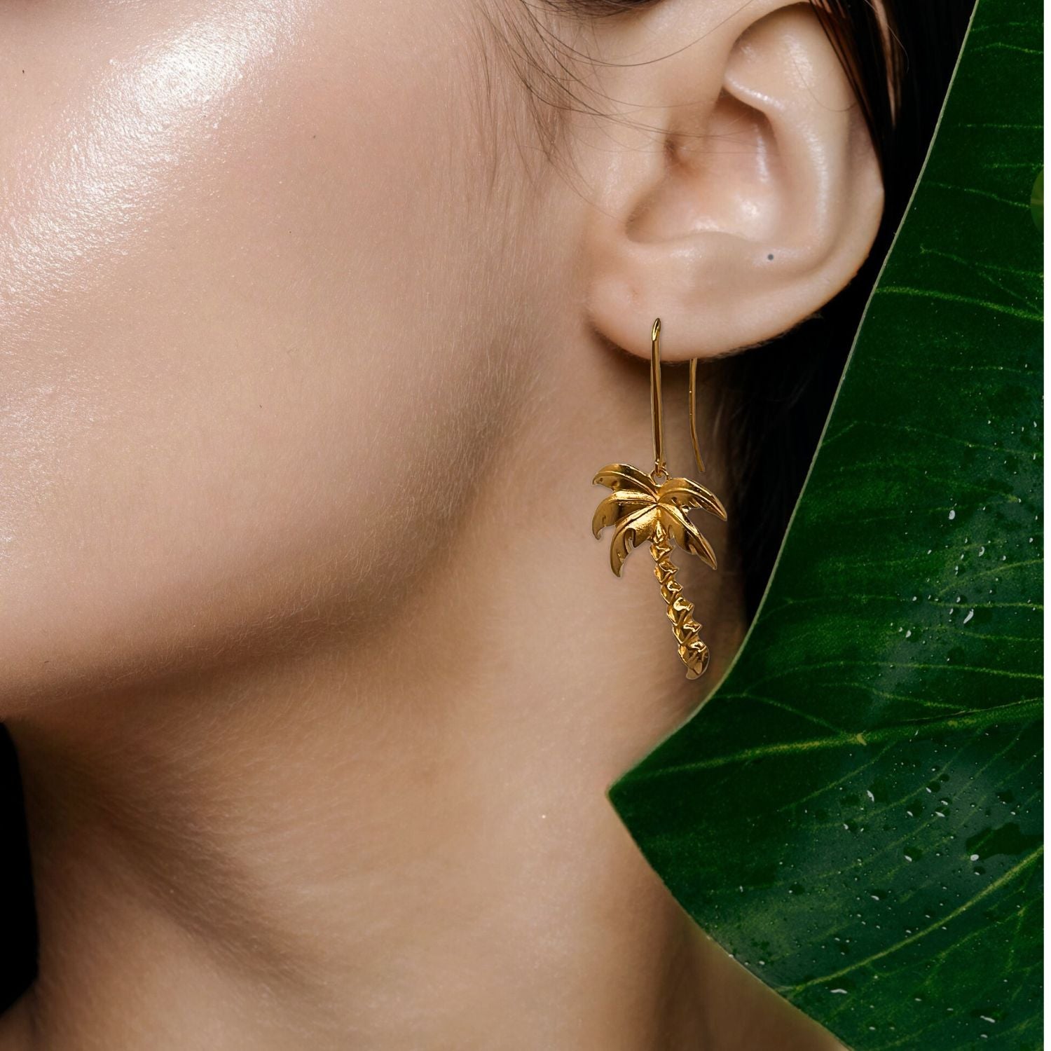 Two Gold Angeleno Palm Hook Earrings by JAREDJAMIN Jewelry Online are shown on a white background. Each earring has a detailed trunk and fronds with a hook, evoking a tropical vibe. Shadows below suggest the earrings are slightly elevated.
