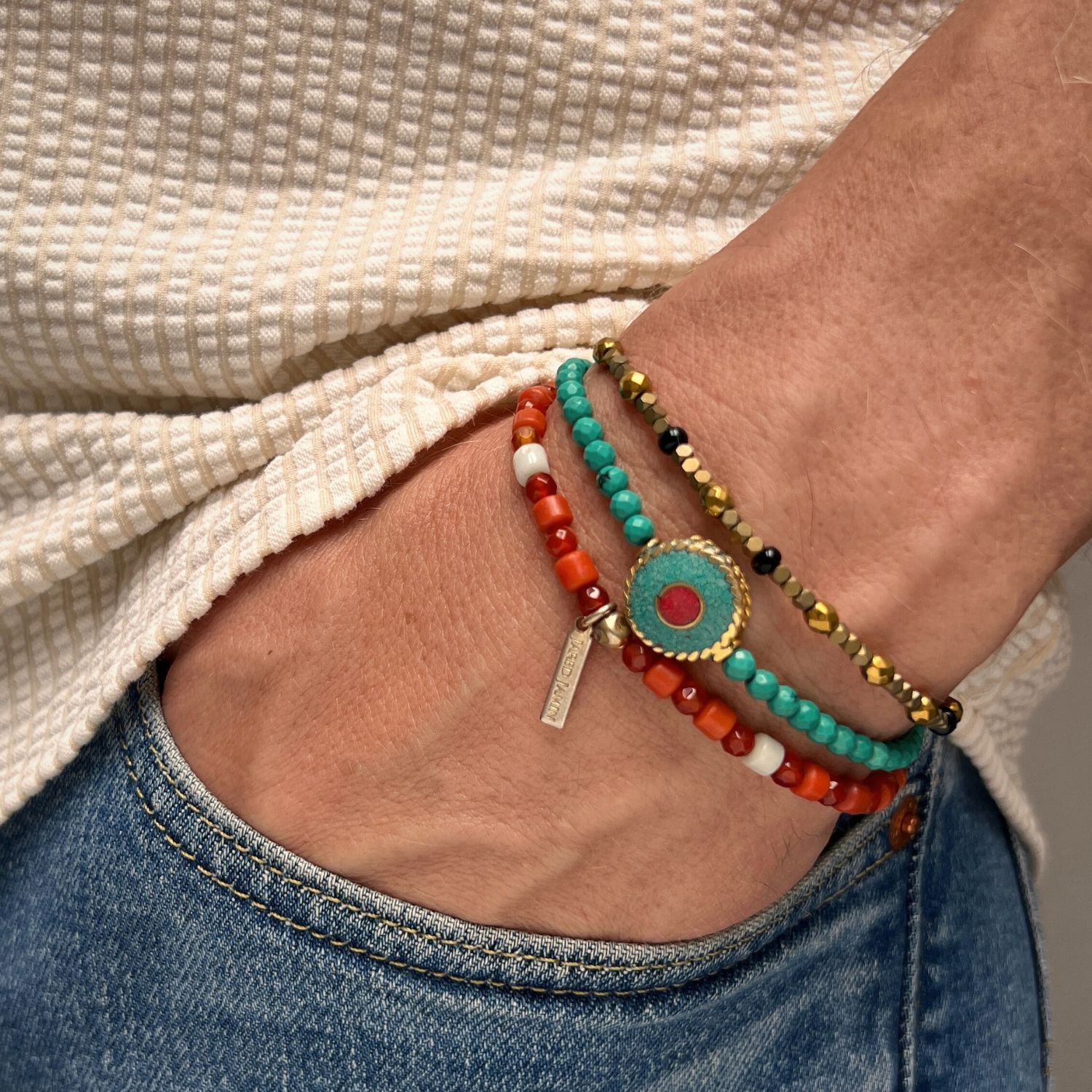 The Aqua Evil Eye Bracelet Set by JAREDJAMIN Jewelry Online features earth-tone beads in turquoise, red, gold, black, and white on a black cord. A round centerpiece with vibrant colors adds bold gemstone-inspired energy to this stylish trio.