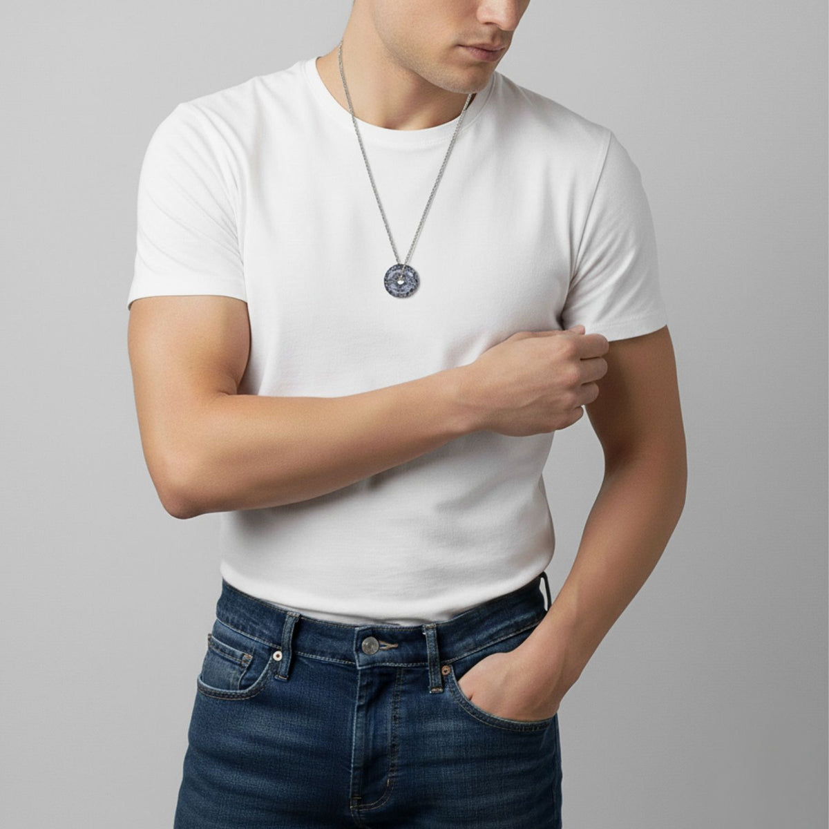 A person in a plain white fitted t-shirt and blue jeans stands against a gray background, wearing the Ash and Or Sterling Silver Necklace by JAREDJAMIN Jewelry Online. They look down, hand on arm, with their face partly visible.
