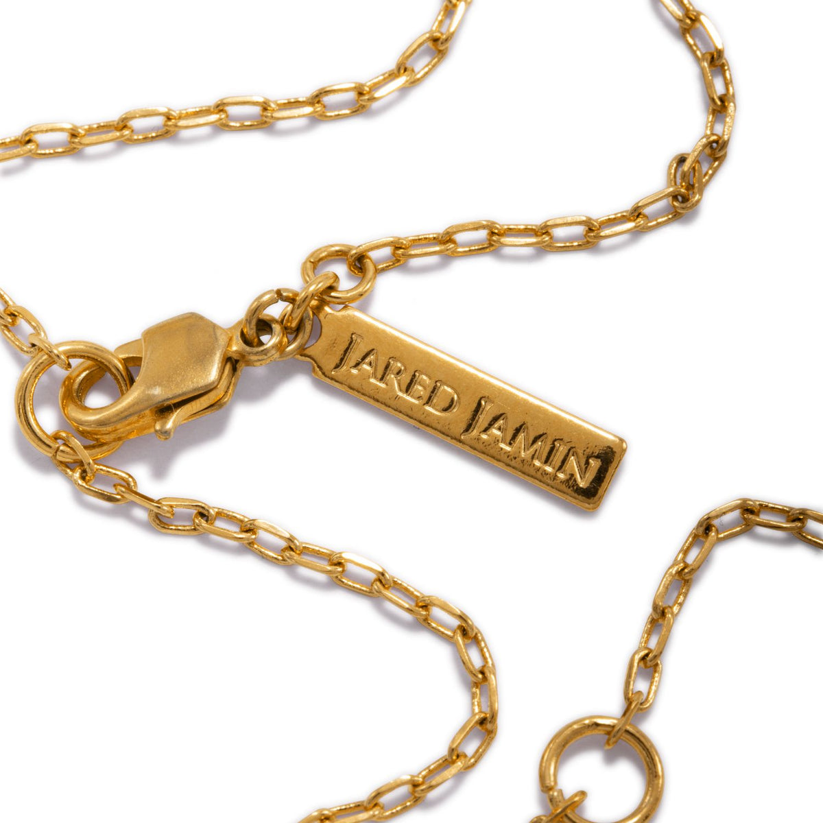 Un primer plano of the Hidden Glimmer colgante collar’s adjustable cadena con elongated links y a lobster clasp. Los rectangular tag is engraved “JAREDJAMIN Joyería Online.” Both the 18k oro cadena y tag rest sobre un fondo blanco.