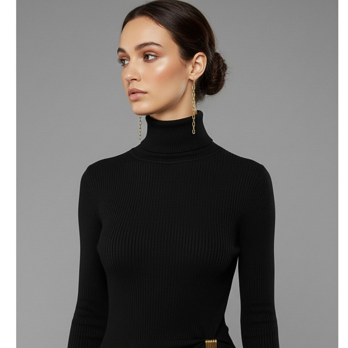Un woman avec dark hair dans un low bun wears a fitted black turtleneck et JAREDJAMIN Bijoux en Ligne's chaîne Reaction Dangle Post boucles d'oreilles. She gazes left, her minimalist style highlighted by the plain gray background.