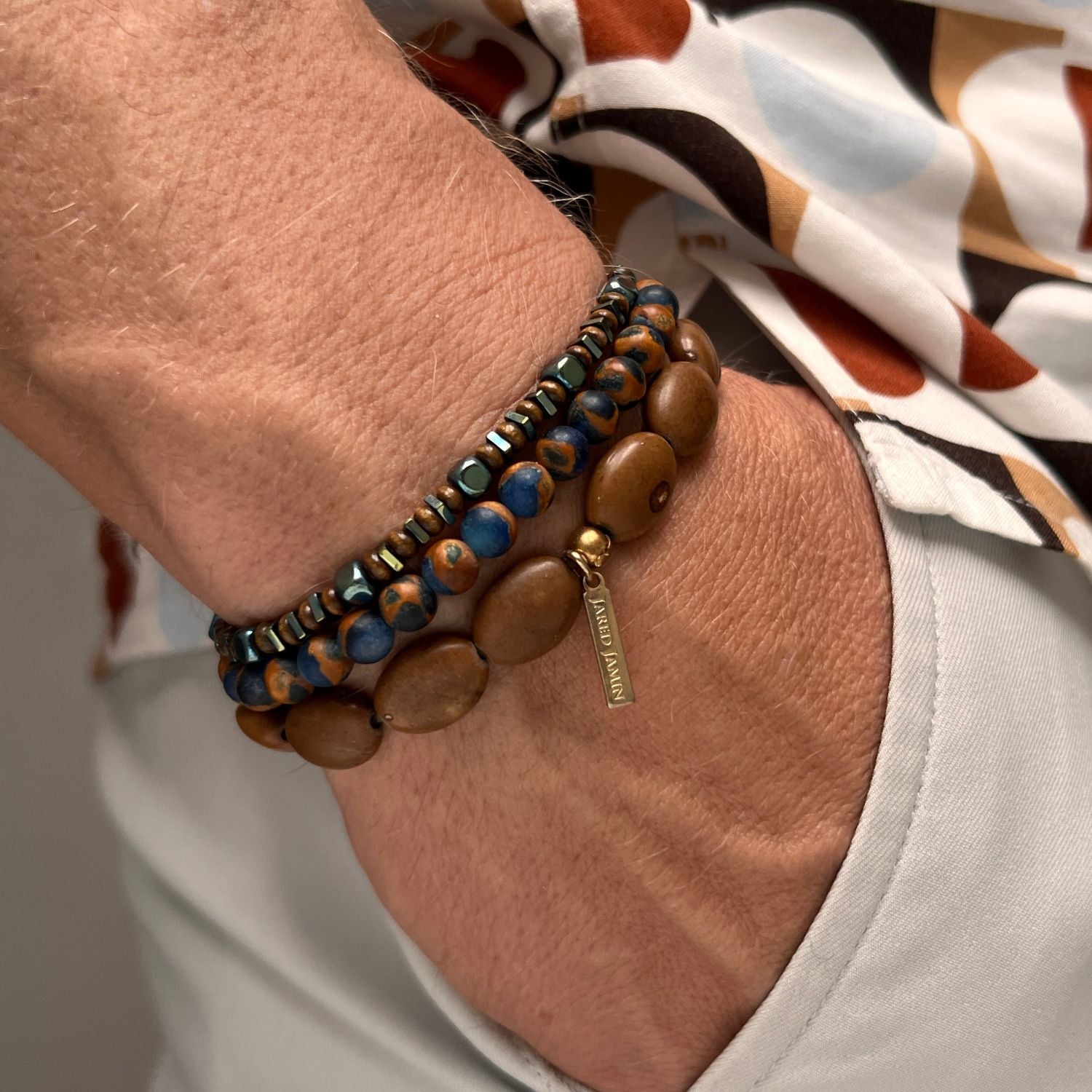 The Coffee King Bracelet Set from JAREDJAMIN Jewelry Online features two coiled strands: one with large oval brown wooden beads, the other with smaller mixed beads in brown, black, blue, metallic tones and accented with freshwater pearls.
