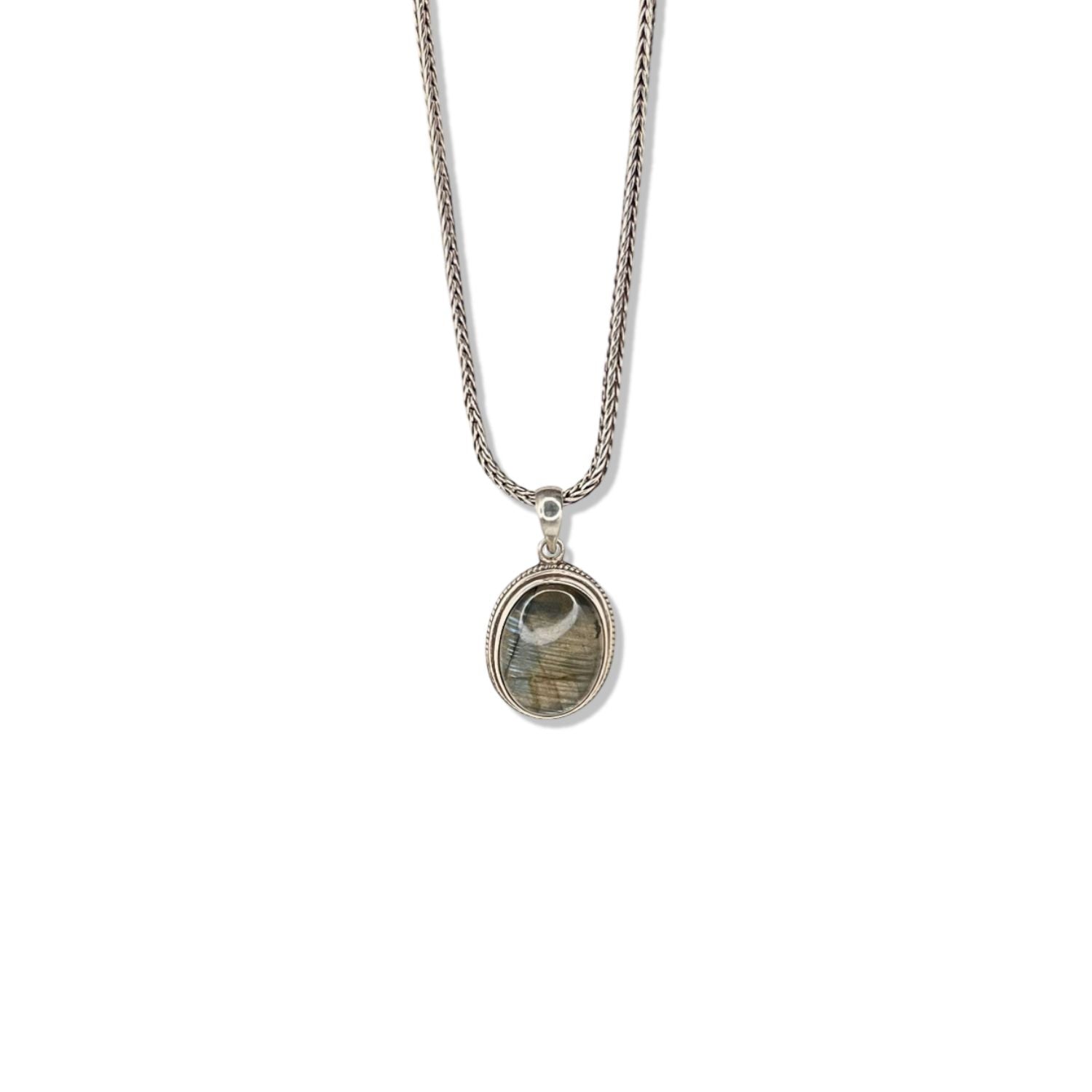 The Confidence Boost Necklace by JAREDJAMIN Jewelry Online features a sterling silver braided chain and a striking oval labradorite pendant, its dark stone streaked with gray, green, and beige for an elegant, uplifting look.