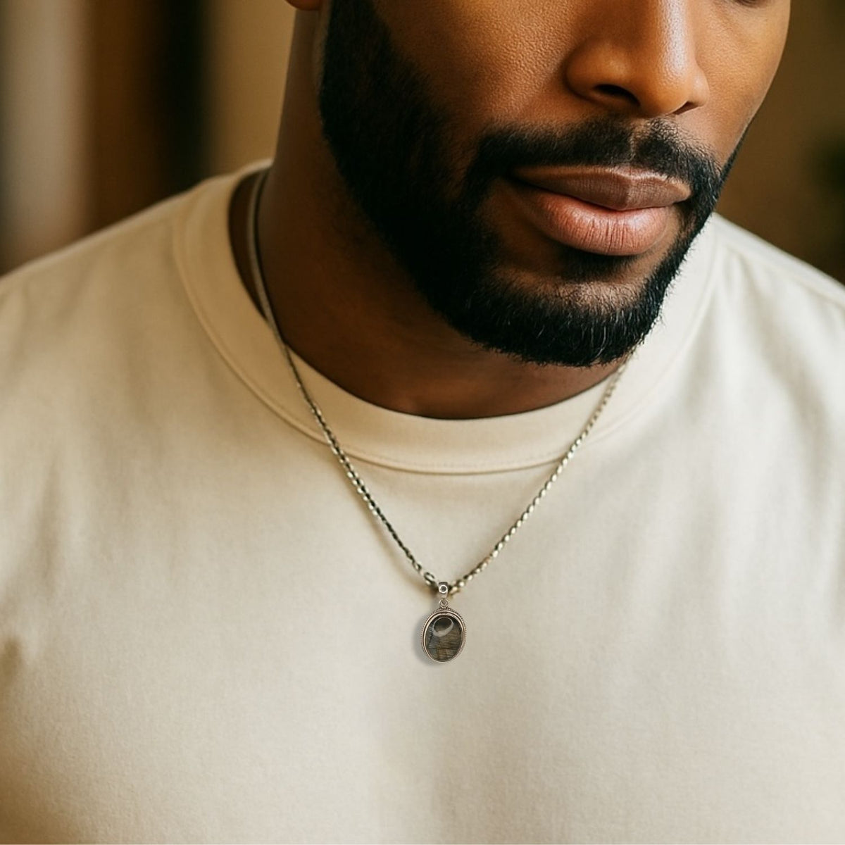 A man with a neatly trimmed beard wears a plain beige t-shirt and the Confidence Boost Necklace by JAREDJAMIN Jewelry Online, featuring labradorite on a sterling silver chain. The cropped image shows his lower face and chest against a softly blurred background.