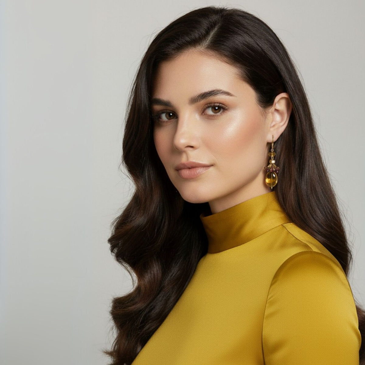 Un woman avec long, wavy dark hair poses dans un mustard yellow turtleneck, wearing JAREDJAMIN Bijoux en Ligne’s Copacabana Dangle boucles d'oreilles. Her soft, glowing makeup et calm confidence stand out against a plain neutral background.