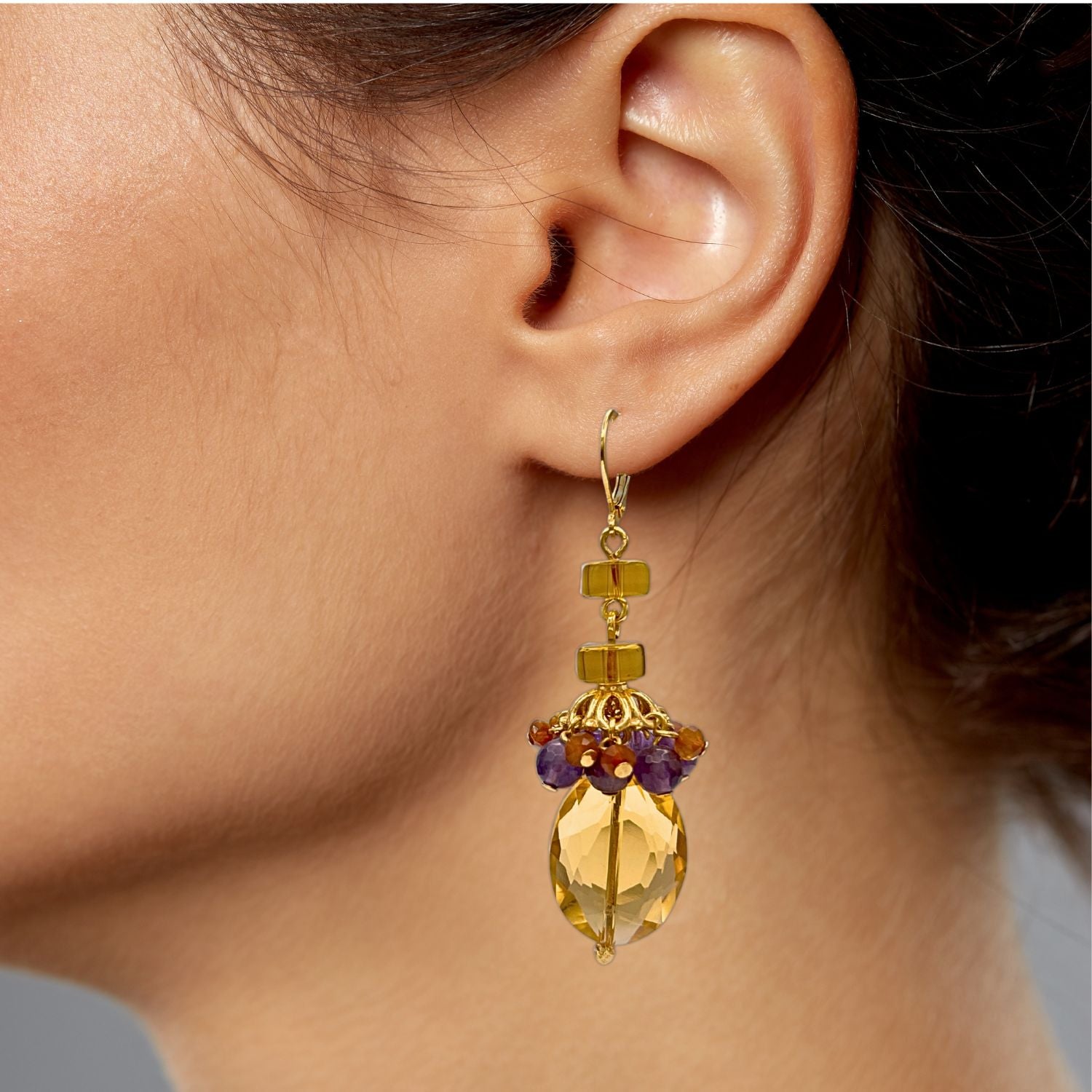 The Copacabana Dangle Earrings by JAREDJAMIN Jewelry Online feature 18K gold plating, faceted yellow oval stones, gold beads, and clusters of small purple and brown beads with lever-back hooks. Shown on a white background.