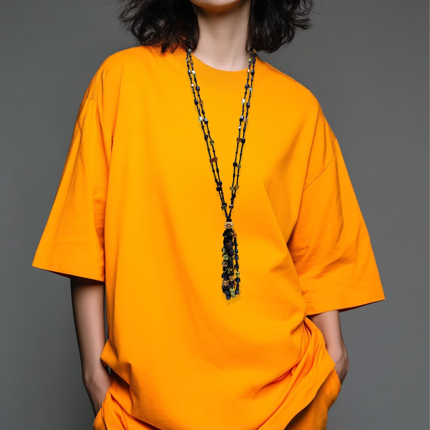 The Cubism Tassel Necklace by JAREDJAMIN Jewelry Online features two black strands with yellow, orange, green, and purple beads, joined at a geometric gold bead and finished with a matching tassel and gold toggle clasp.