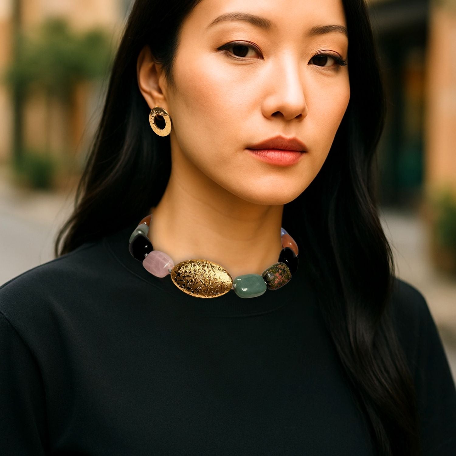 The Earthen Elegance Gemstone Necklace by JAREDJAMIN Jewelry Online displays multicolored rectangular aventurine and rose quartz beads with a large engraved gold oval bead and gold toggle clasp, arranged in a circle on a white background.