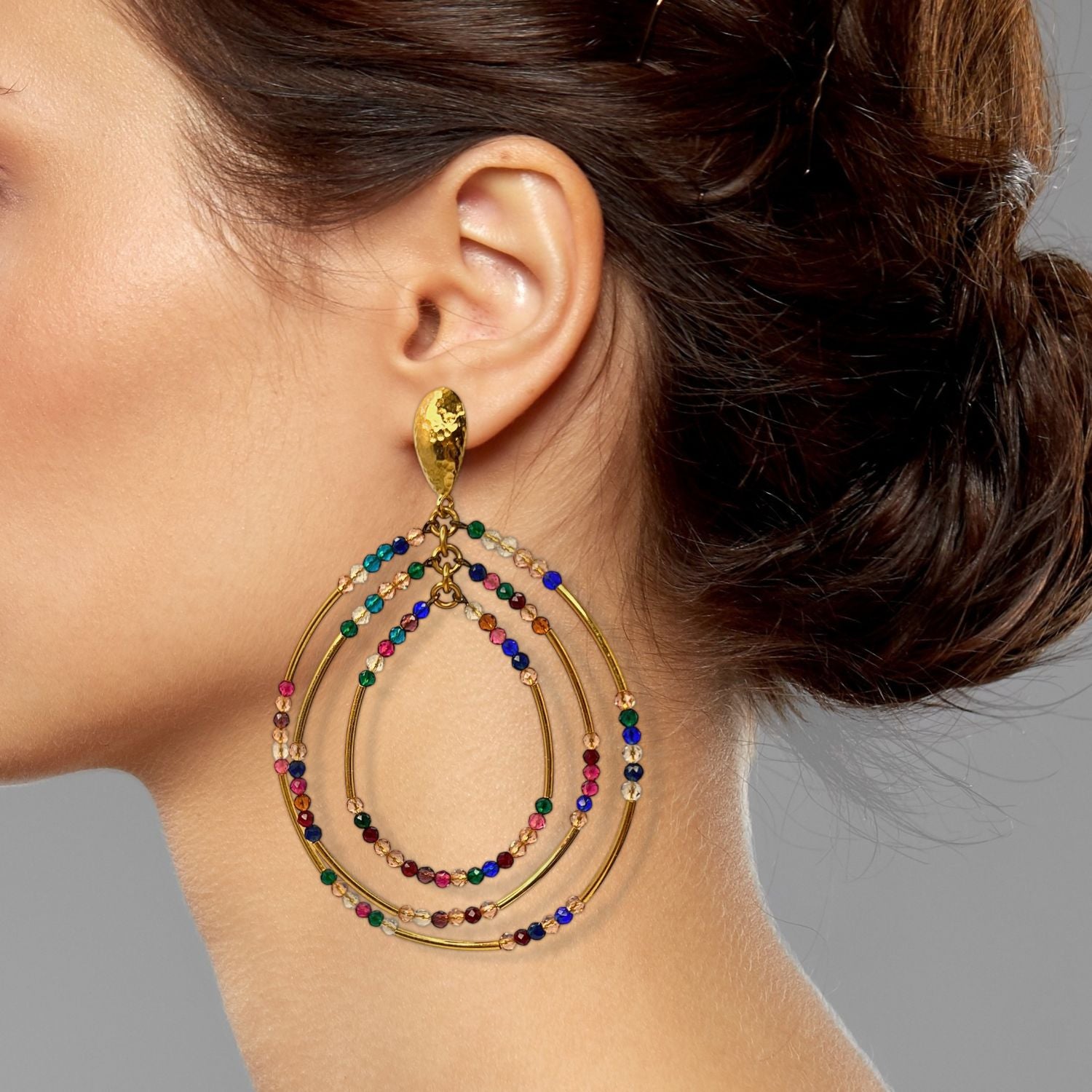 The Easy Breezy Multicolor Post Earrings from JAREDJAMIN Jewelry Online feature gold-plated dangle earrings with three overlapping teardrop hoops, adorned with blue, green, red, brown, and white beads on hammered gold teardrop studs.
