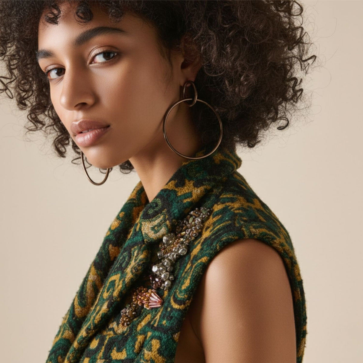 Un young woman avec curly hair et a calm, confident expression wears Everly Antique Dangle créole Post boucles d'oreilles par JAREDJAMIN Bijoux en Ligne. She pairs them avec a green et yellow sleeveless beaded top, set against a soft beige background.