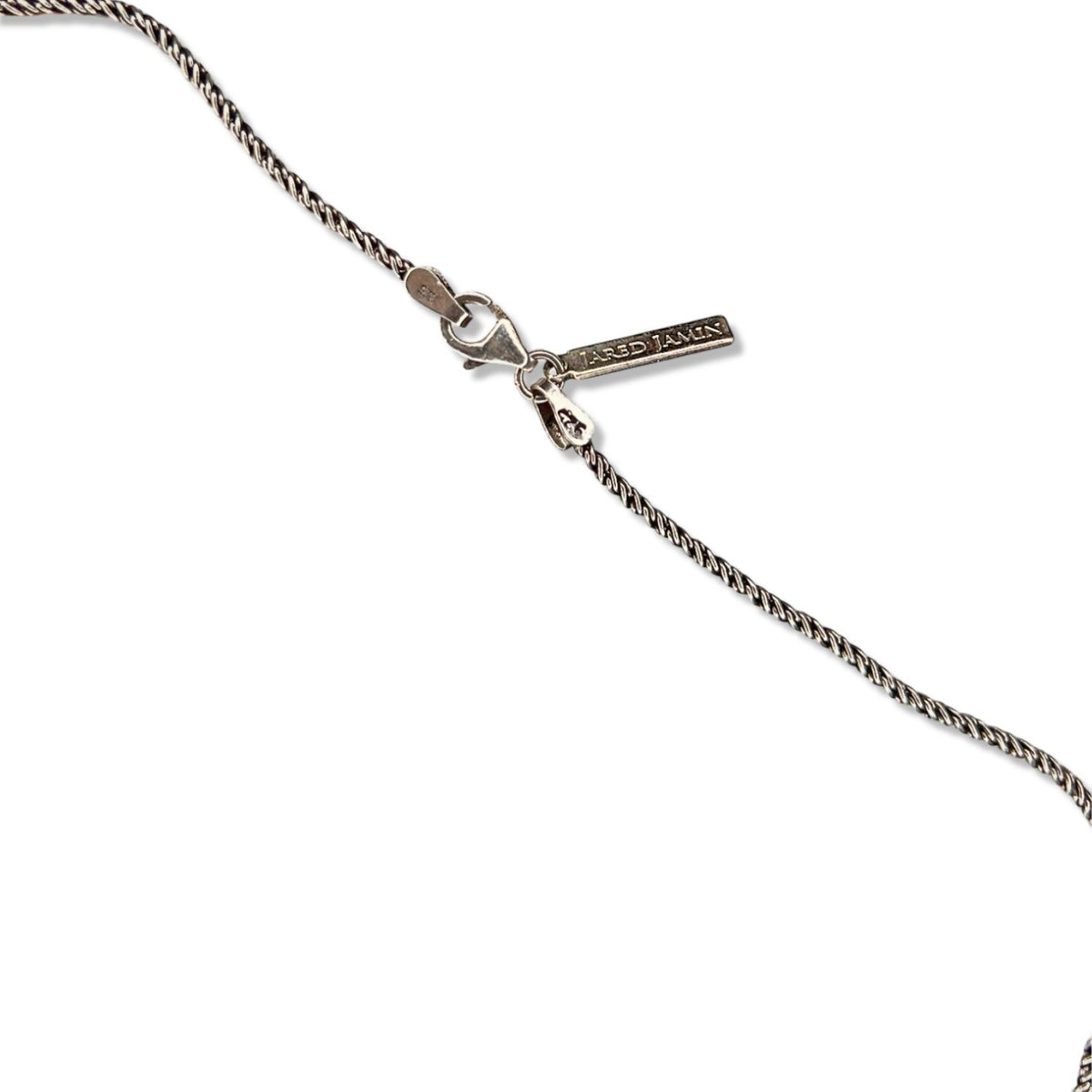 A close-up of the Gage Garnet Necklace by JAREDJAMIN Jewelry Online, featuring a twisted sterling silver chain, lobster clasp, an oval “925” tag, and a rectangular “JAREDJAMIN” tag against a white background.