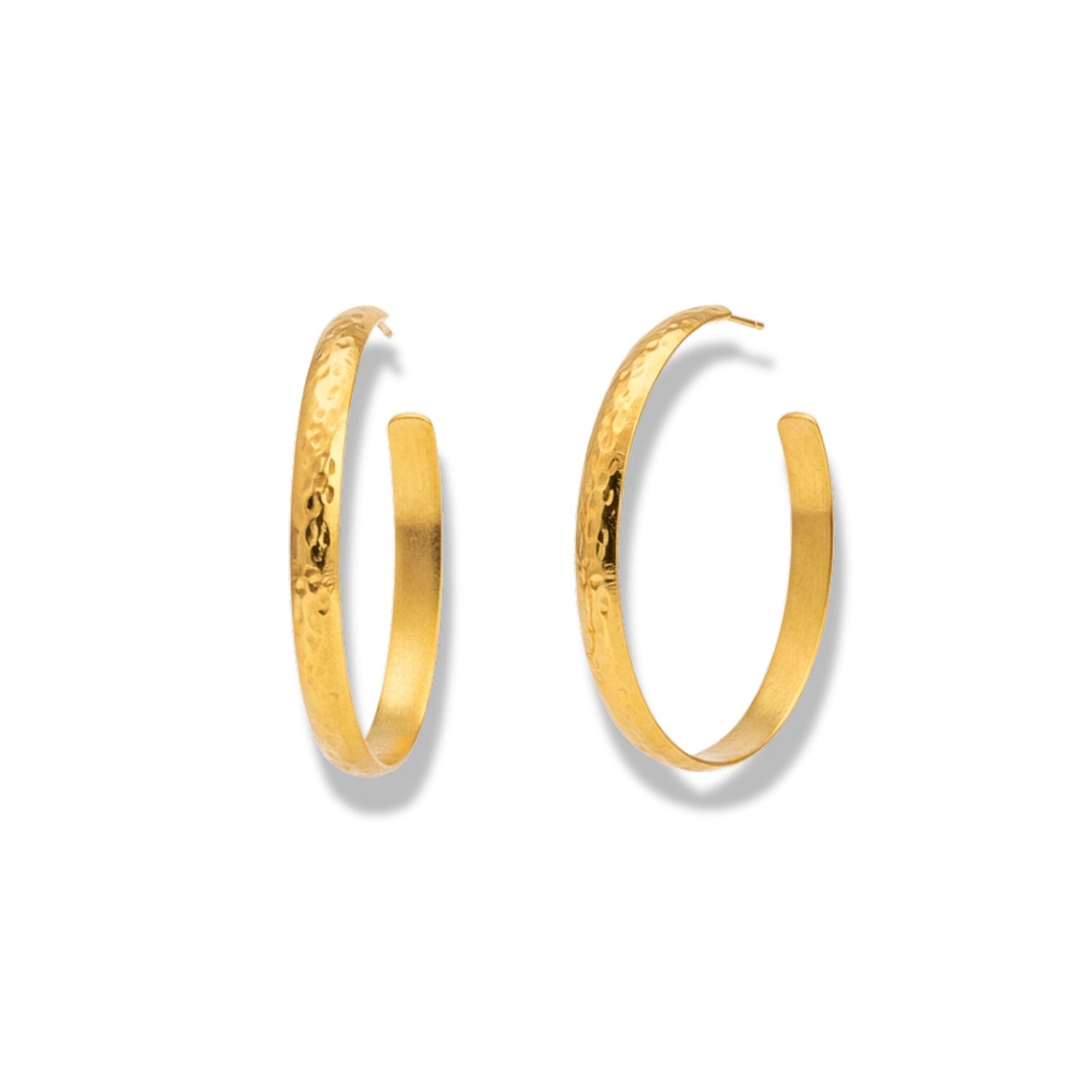 The Galilea Textured Hoop Post Earrings by JAREDJAMIN Jewelry Online feature medium-sized, hammered gold hoops with a wide, flat surface that reflects light. Each open-back earring forms a partial circle and casts a shadow beneath.