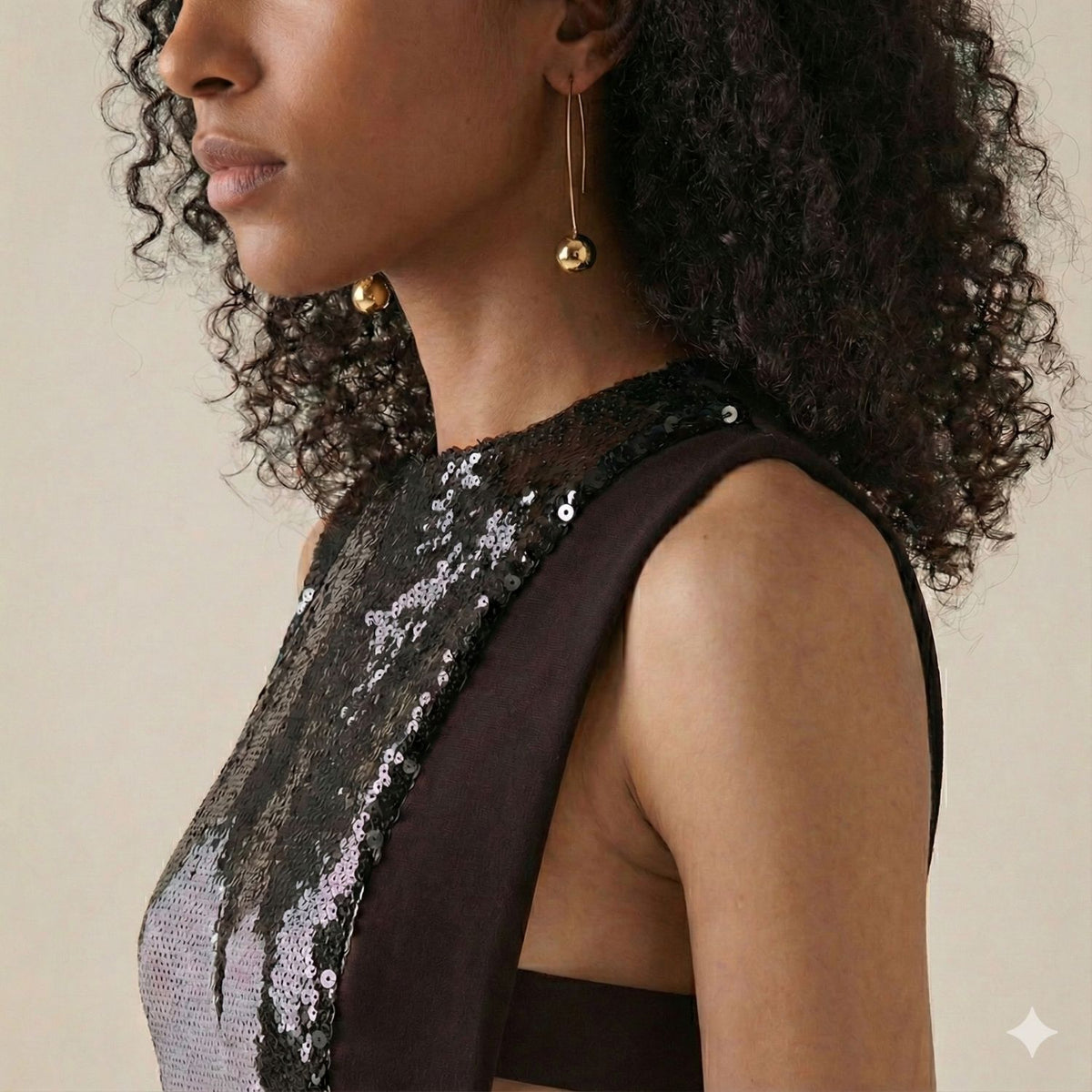 Un woman avec curly hair wears a sleeveless black sequin dress, facing left dans un neutral pose against a beige background. She accessorizes avec élégant Cherry Hook boucles d'oreilles par JAREDJAMIN Bijoux en Ligne.