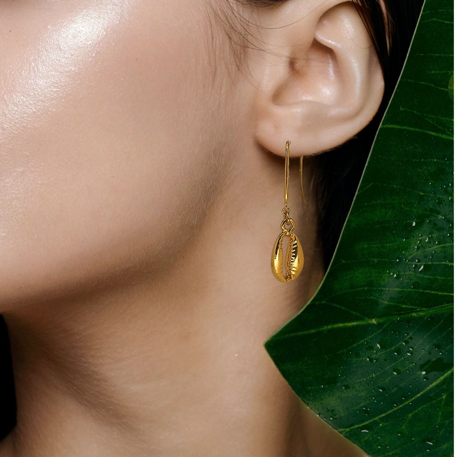 The Gold Cowrie French Hook Earrings by JAREDJAMIN Jewelry Online feature polished brass shells with detailed grooves, hanging from simple hooks. Shown on a plain white background.