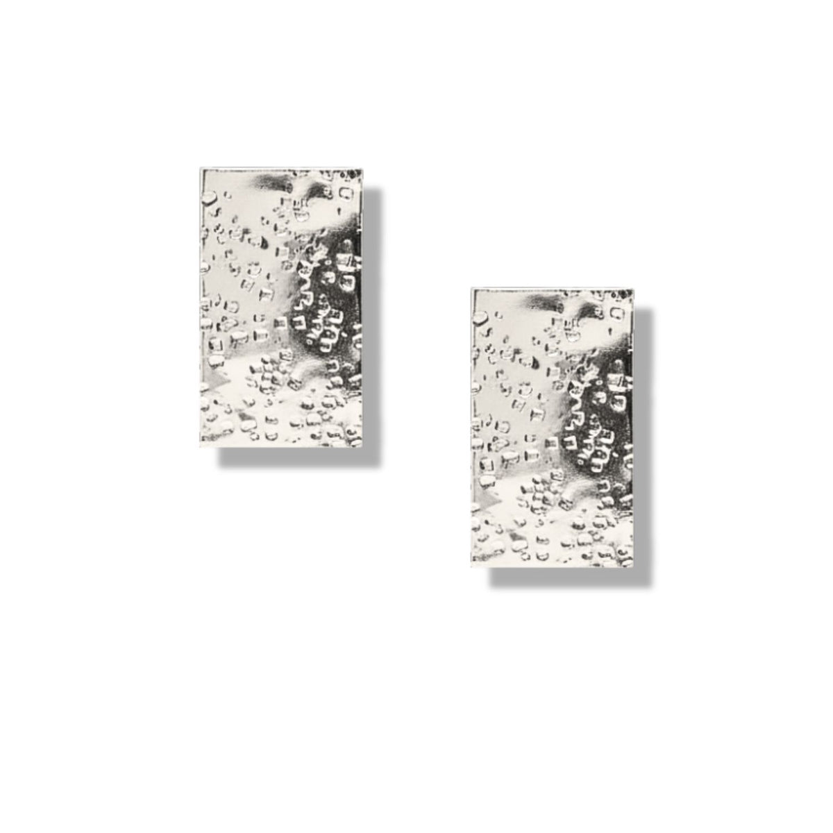 The Gold Cuszco Post Earrings by JAREDJAMIN feature a hammered texture that resembles water droplets. Each rectangular earring casts a soft shadow on white, showcasing their glossy, reflective gold finish.