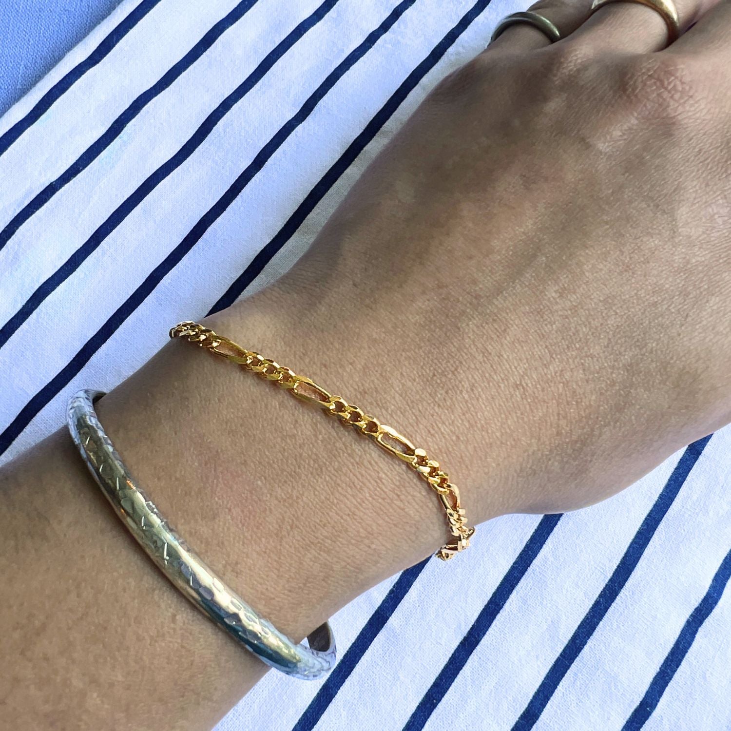 The Gold Finley-Figaro Chain Bracelet by JAREDJAMIN Jewelry Online features delicate interlocking 18K gold plated links, a JARED JAMES engraved tag, and a secure lobster clasp, shown on a white background.