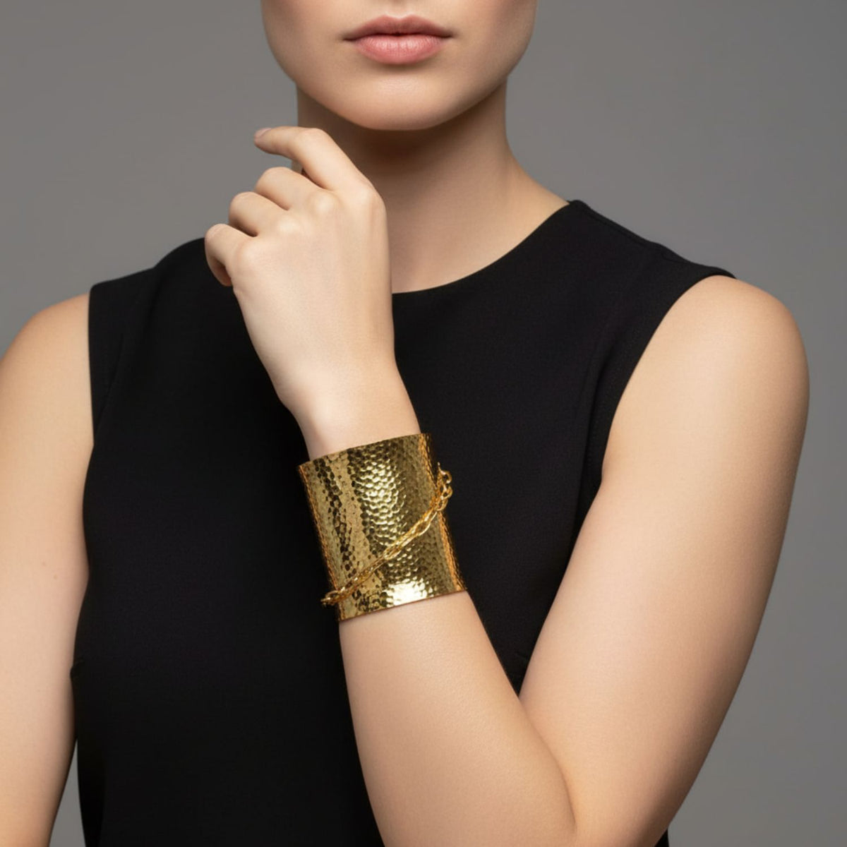 Un woman dans un sleeveless black top poses avec her hand near her chin, highlighting the Galilea texturé manchette bracelet par JAREDJAMIN Bijoux en Ligne. Les plain gray background emphasizes the bracelet et her élégant, minimalistic style.