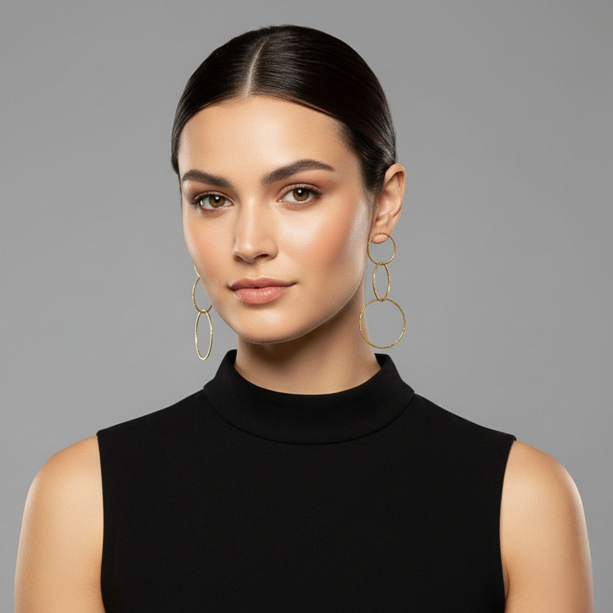 Un woman avec smooth dark hair, parted center, wears JAREDJAMIN Bijoux en Ligne’s or Lindy Links Post boucles d'oreilles et a sleeveless black turtleneck. She faces forward against a plain gray background avec calm expression et natural makeup.