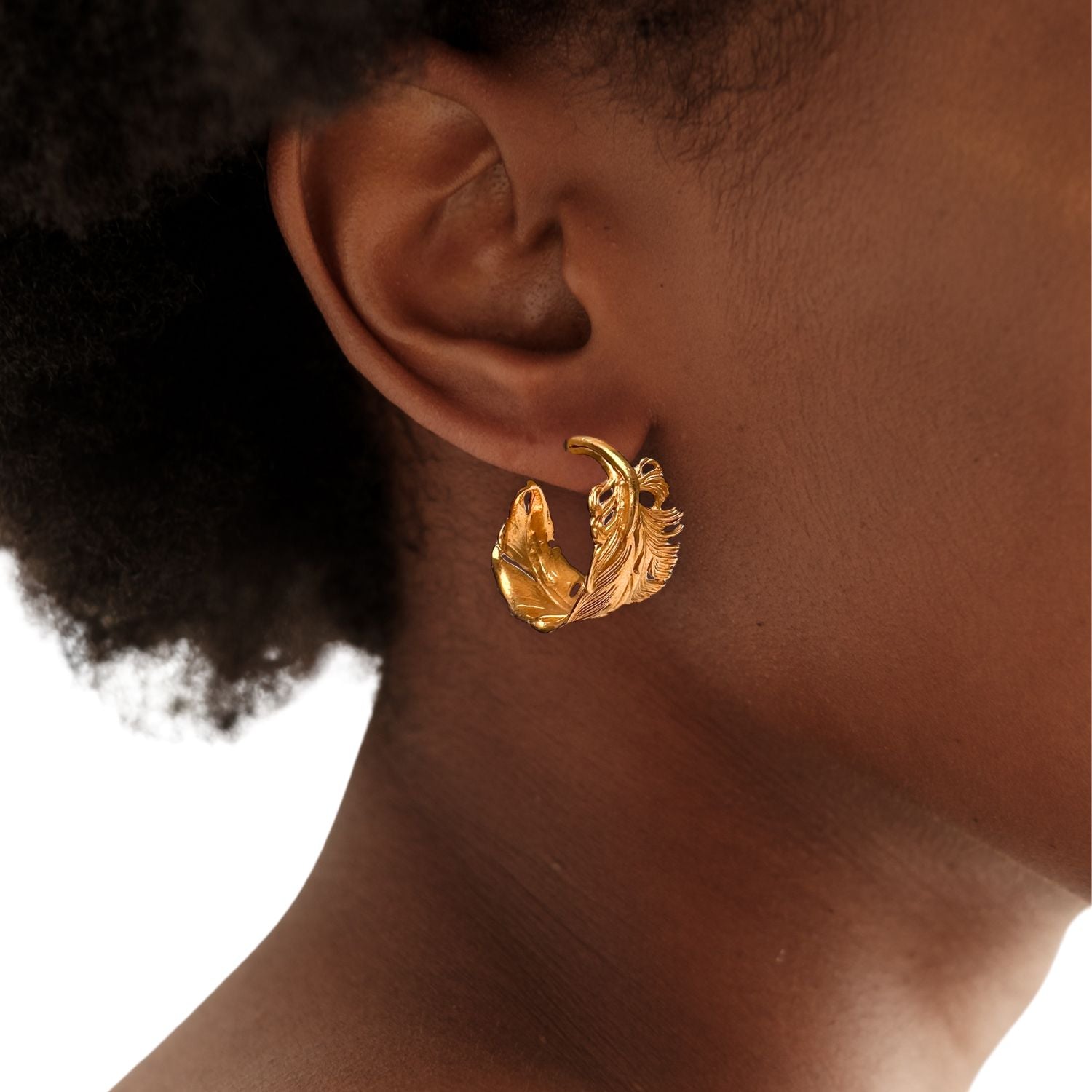 The Gold Plume Hoop Post Earrings by JAREDJAMIN Jewelry Online feature detailed, textured leaf designs with intricate veins and edges, resembling golden feathers. Shown upright on a white background, they cast soft right-facing shadows.