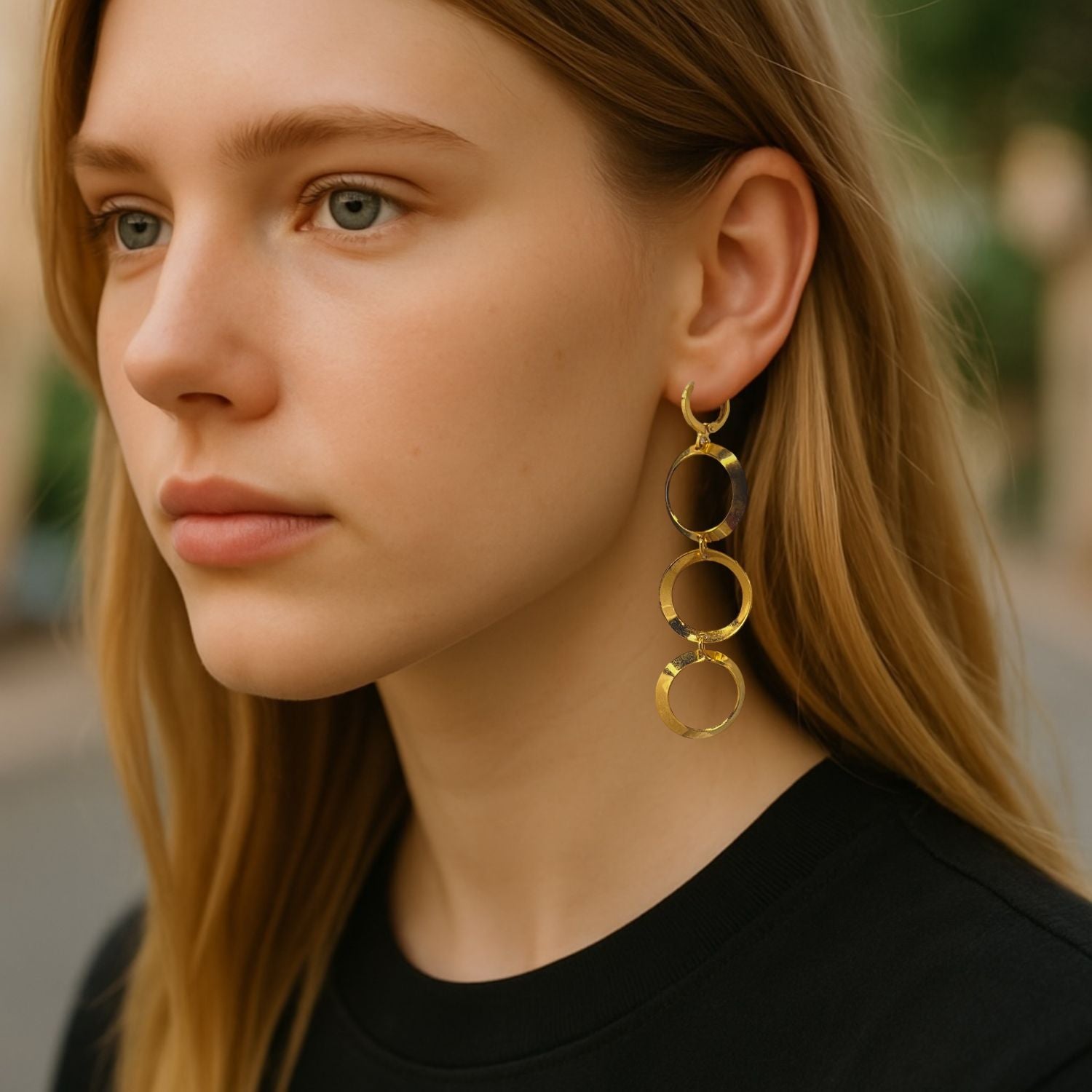 The Gold Rimini Loop Earrings from JAREDJAMIN Jewelry Online are 18K gold plated dangle earrings with three interlocking shiny hoops linked vertically for a cascading effect. Lightweight with hinged hoop closures. Plain white background.