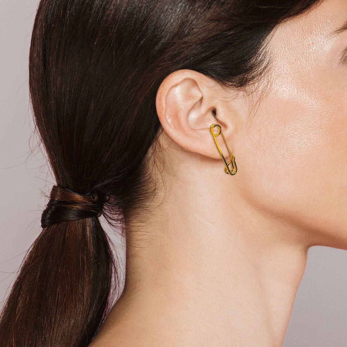 A womanとstraight brown hair の中の low ponytail is shown in profile against a plain background, wearing JAREDJAMIN ジュエリーオンライン’s ゴールド Safety First Post イヤリング, crafted from 18K ゴールド Plate 付きの surgical steel post.