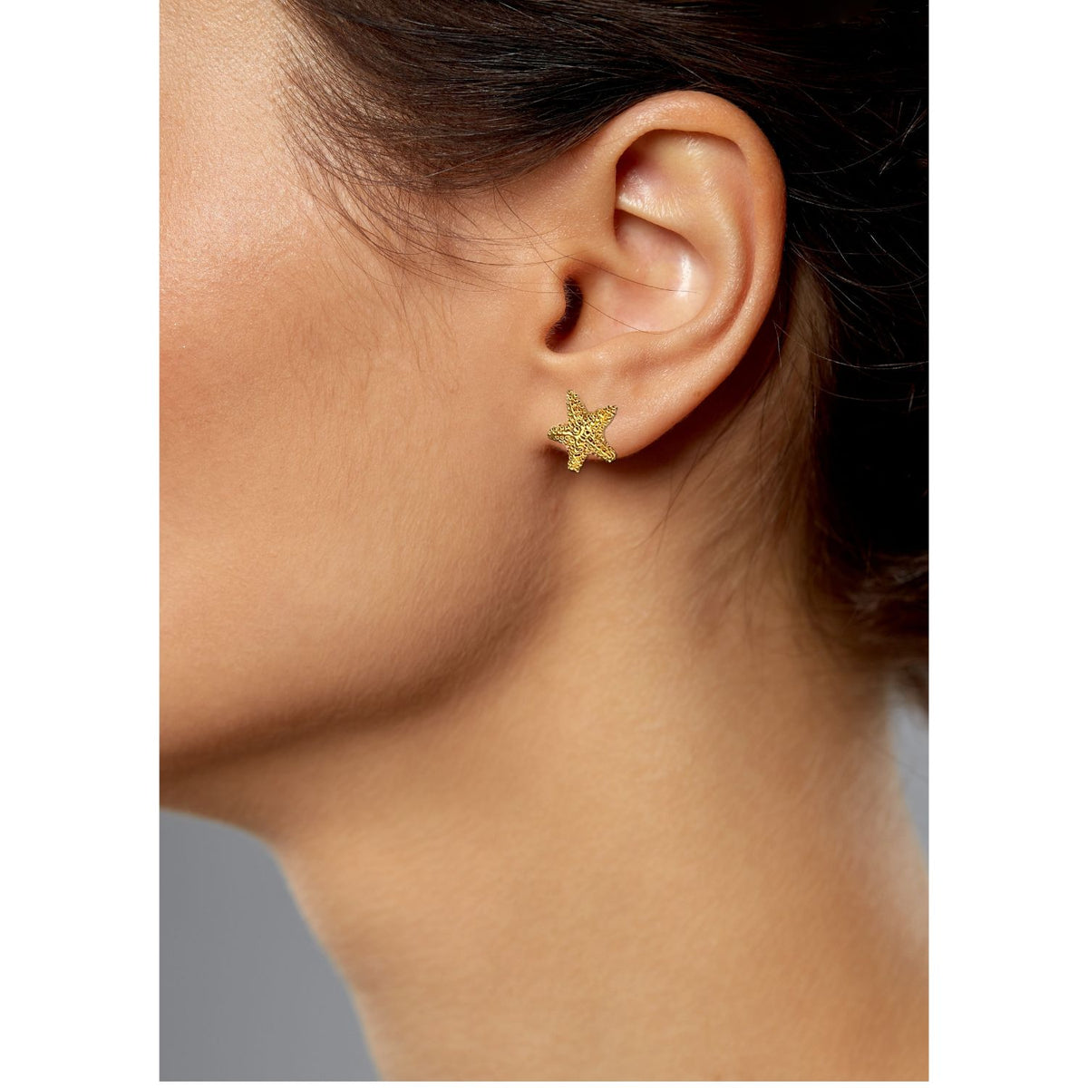 gros plan of a femme portant JAREDJAMIN Bijoux en Ligne’s or Sea Star puce Post boucles d'oreilles. Her medium skin et dark hair pulled back highlight the délicat, plaqué or seaside design against a smooth, neutral background.