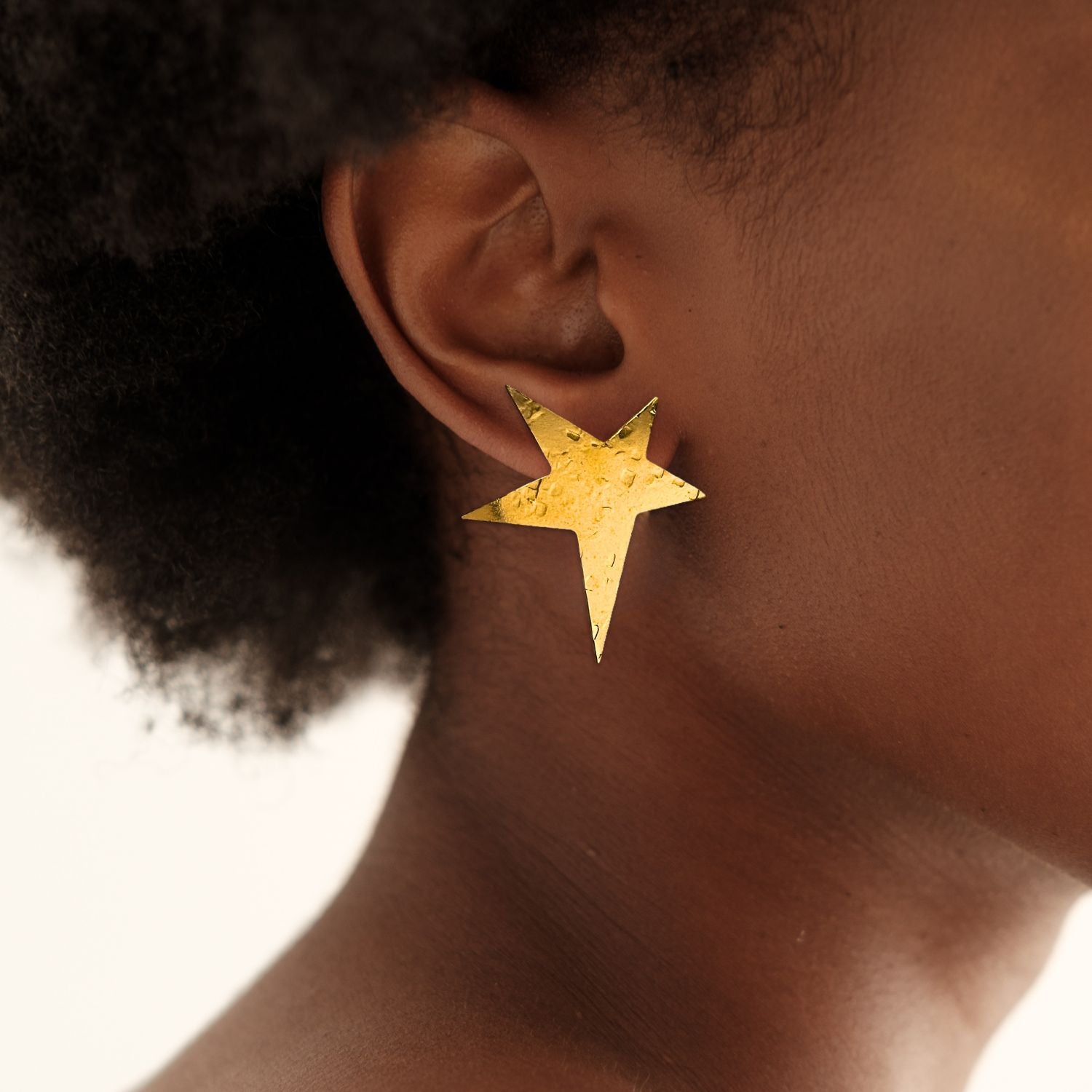 The Gold Shooting Star Clip On Earrings by JAREDJAMIN Jewelry Online feature a hammered, 18K gold-plated finish with five pointed tips—one elongated for a dynamic look. Their textured, reflective surface and irregular dimples add modern flair.