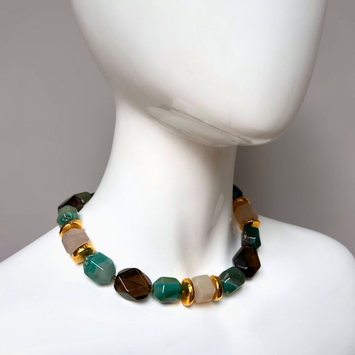 On display is the Green Dream Necklace by JAREDJAMIN Jewelry Online, featuring chunky, hand-knotted beads in green agate, beige, and dark brown. Shiny gold spacers accentuate the design against a white backdrop.