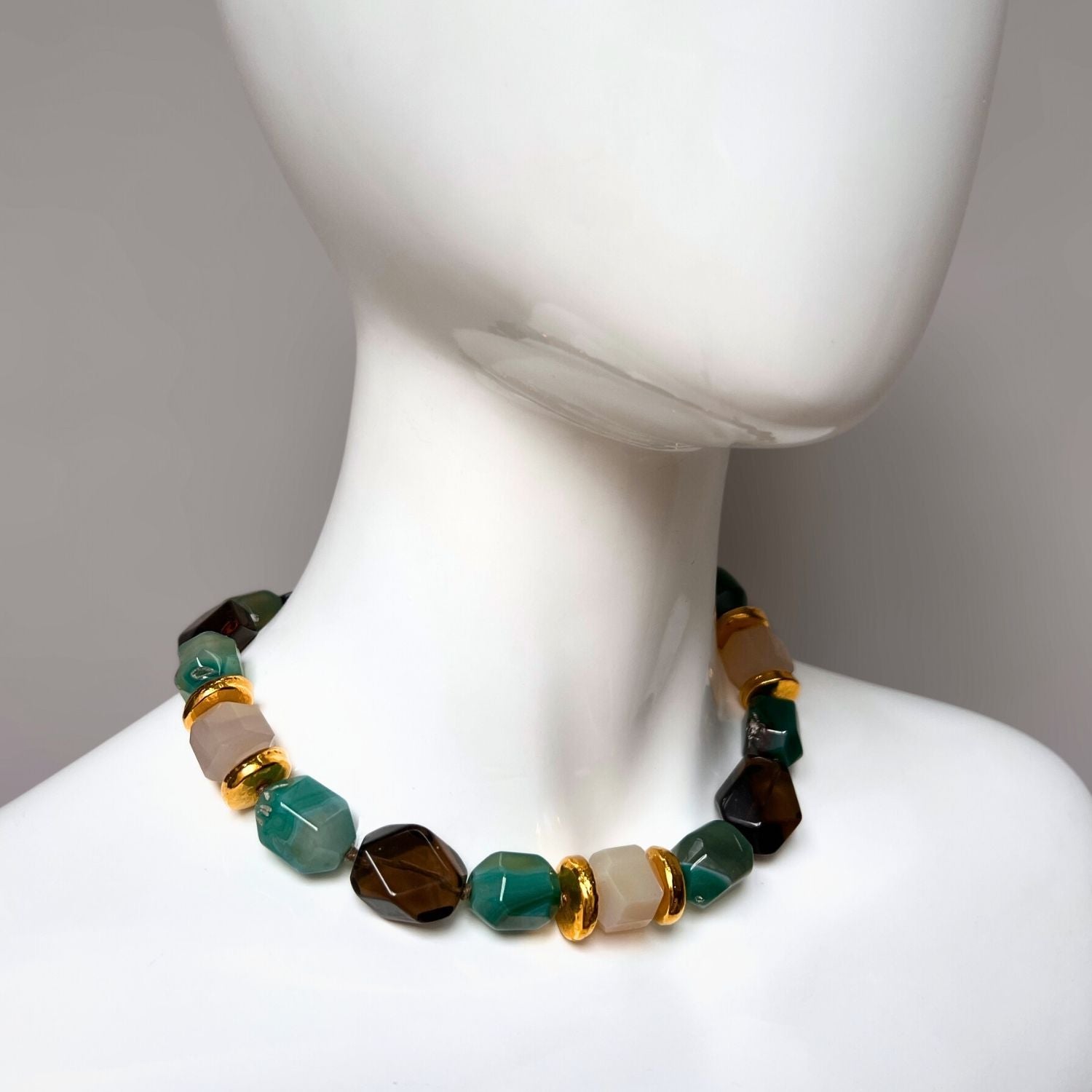 The Green Dream Necklace by JAREDJAMIN Jewelry Online features faceted green agate and stones in brown and beige tones, complemented by gold-tone spacer beads. It includes a gold-tone clasp with an adjustable chain, beautifully arranged in a circle on a white background.