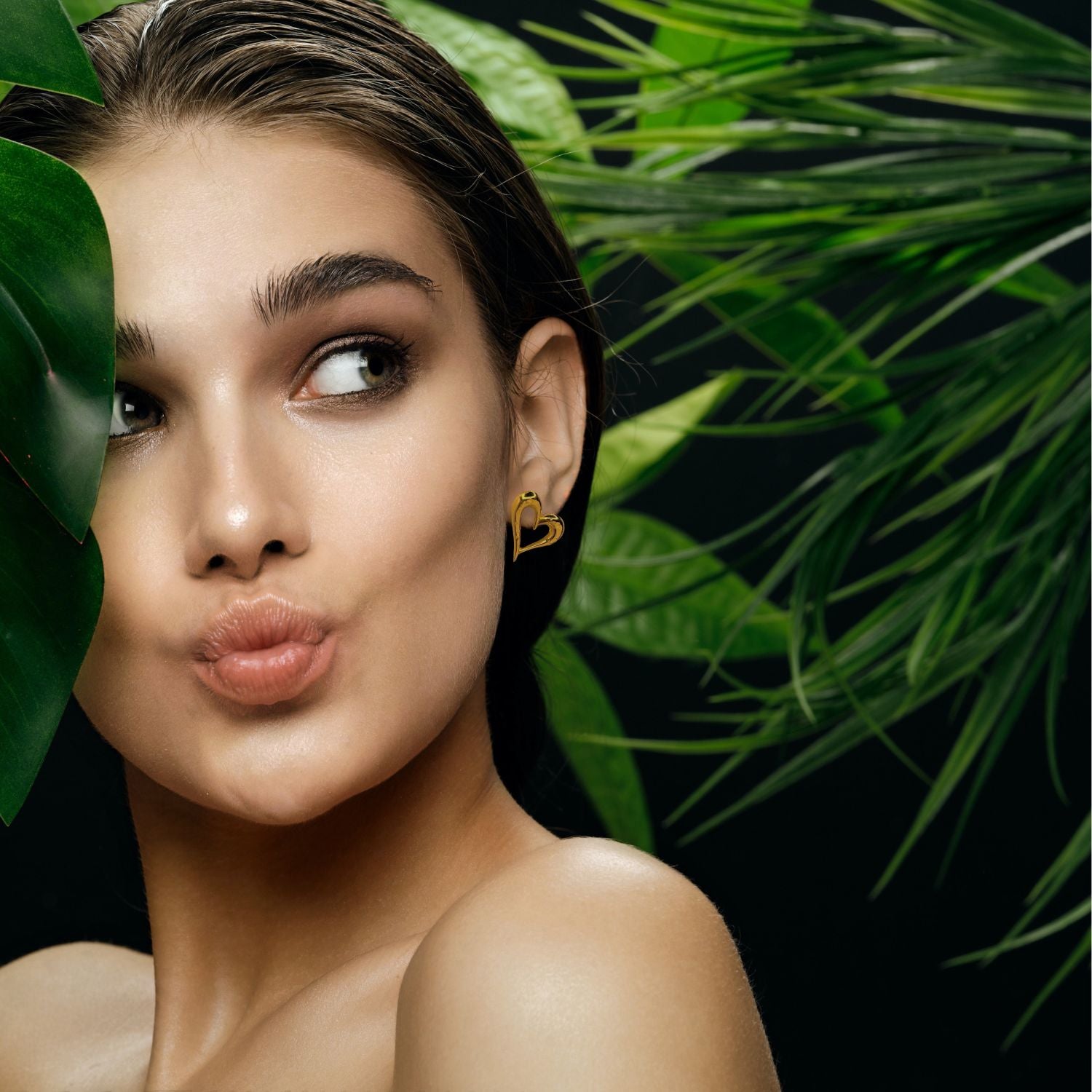 Heartfelt Earrings by JAREDJAMIN Jewelry Online: a pair of shiny gold, heart-shaped earrings with a smooth, reflective finish rest side by side, slightly tilted, casting faint shadows on a white background.