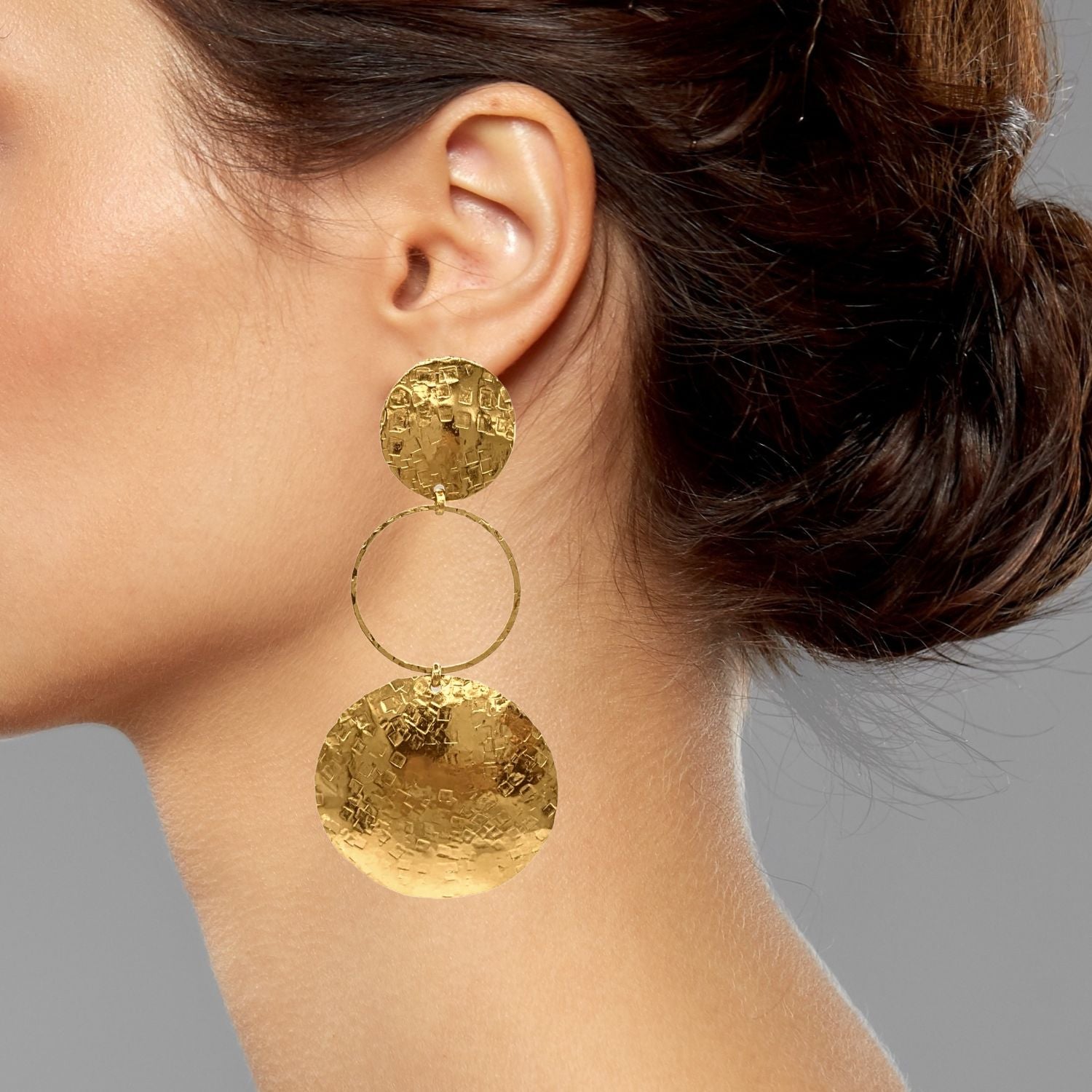 The Hera Textured Clip On Earrings by JAREDJAMIN Jewelry Online feature 18K gold plating, a small textured disc, a thin hoop center, and a larger hammered disc below for a luxe, reflective finish.