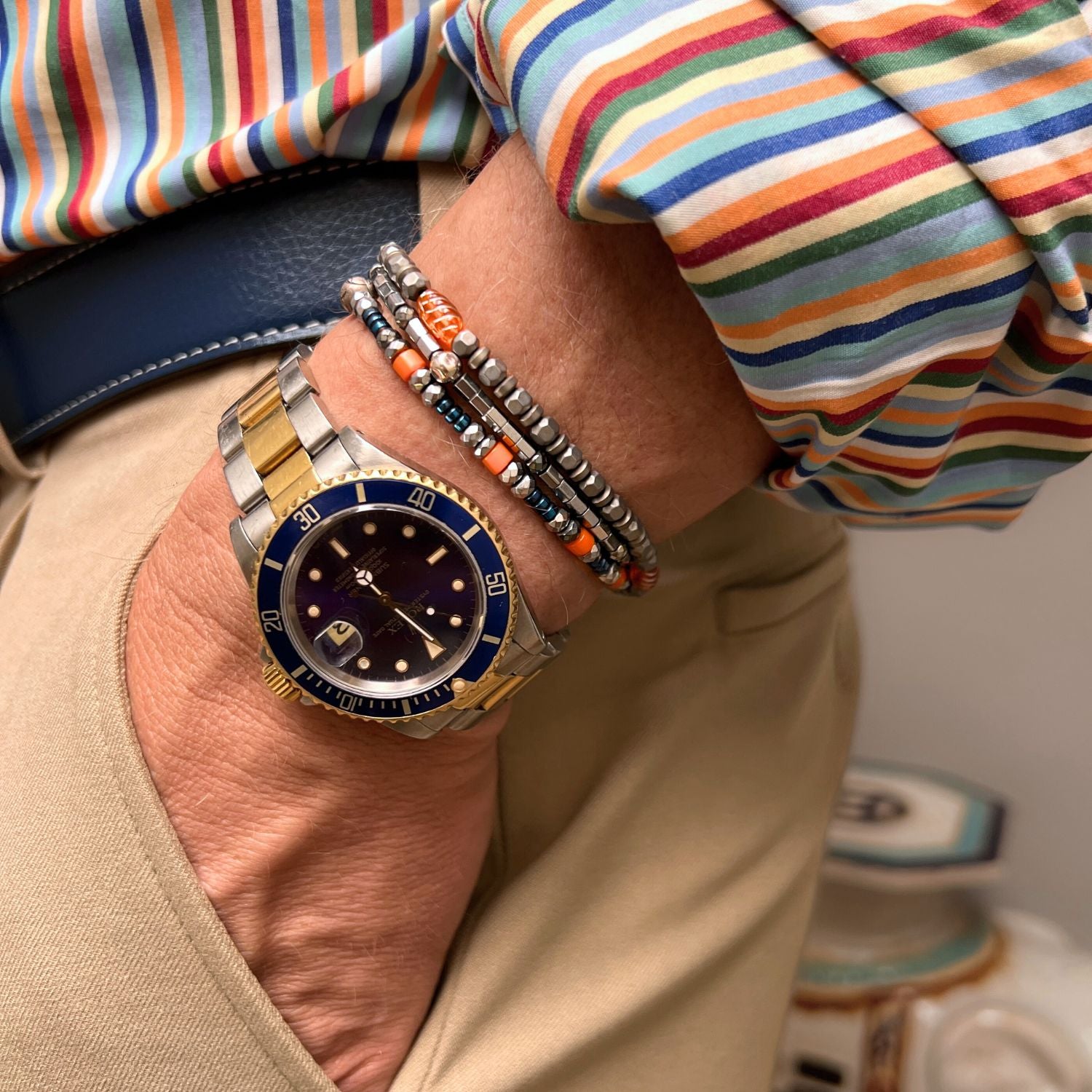 The Hot Rod Apache Bracelet Set by JAREDJAMIN Jewelry Online features multi-strand heishi beads in metallic, gray, blue, and orange with a bold central orange leaf-shaped bead for a layered, textured effect.