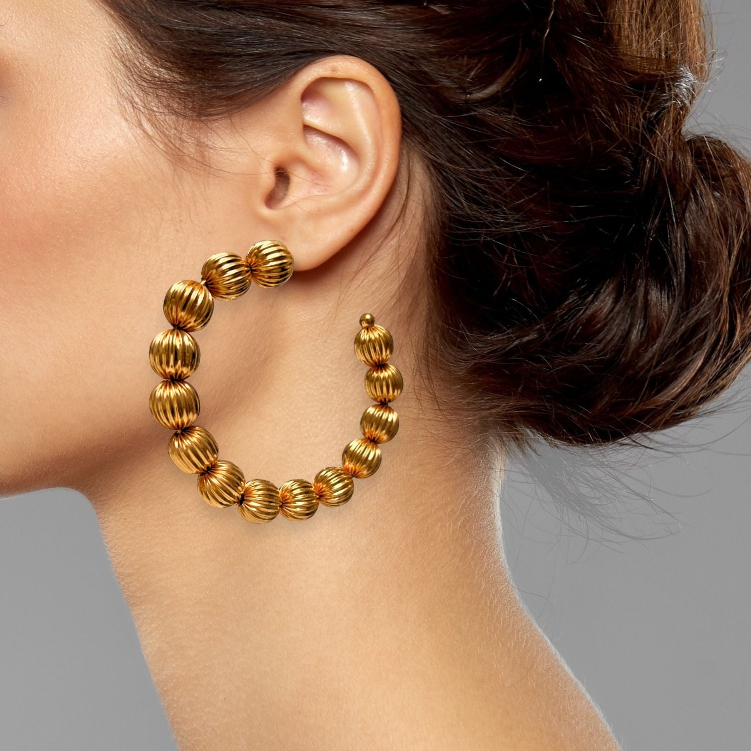 The Large Gold Lantern Hoop Post Earrings by JAREDJAMIN Jewelry Online feature featherweight semi-circles of 18k gold plated, ribbed lantern beads with a shiny finish and thin posts for easy fastening.