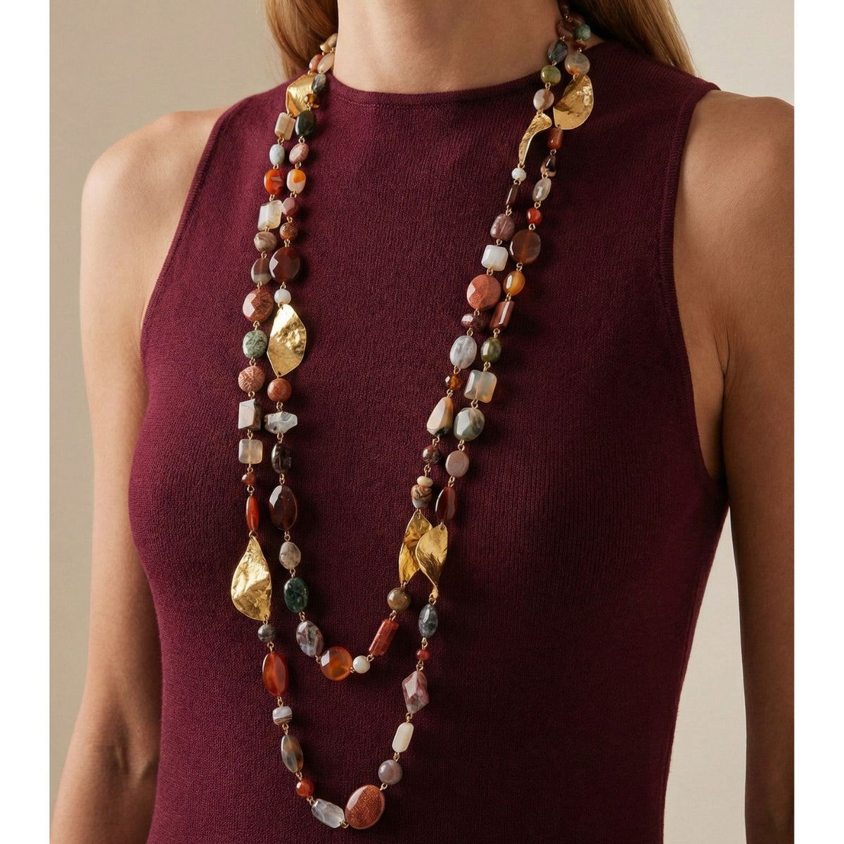A person in a sleeveless burgundy top wears two long Geo Twist Gemstone Linked Necklaces by JAREDJAMIN Jewelry Online, featuring colorful jasper agate quartz stones and gold leaf accents. Background is neutral.