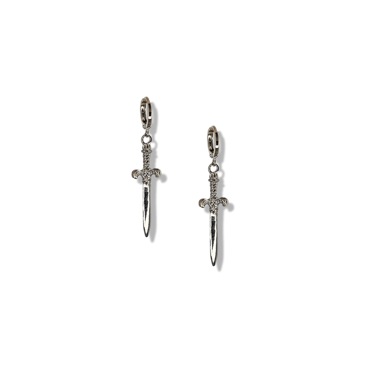 The Silver Macbeth Dangle Earrings by JAREDJAMIN Jewelry Online feature two silver-plated daggers with intricate hilts and blades, hanging vertically from hoops for a bold, detailed metallic look.